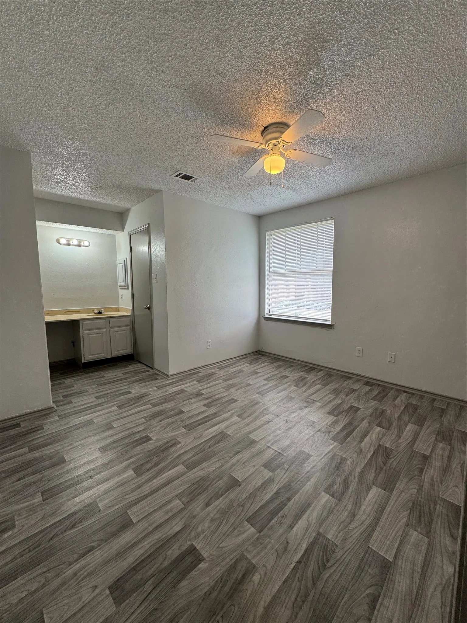 Spacious interior featuring wood-finish flooring, a ceiling fan with integrated lighting, and a window with blinds
