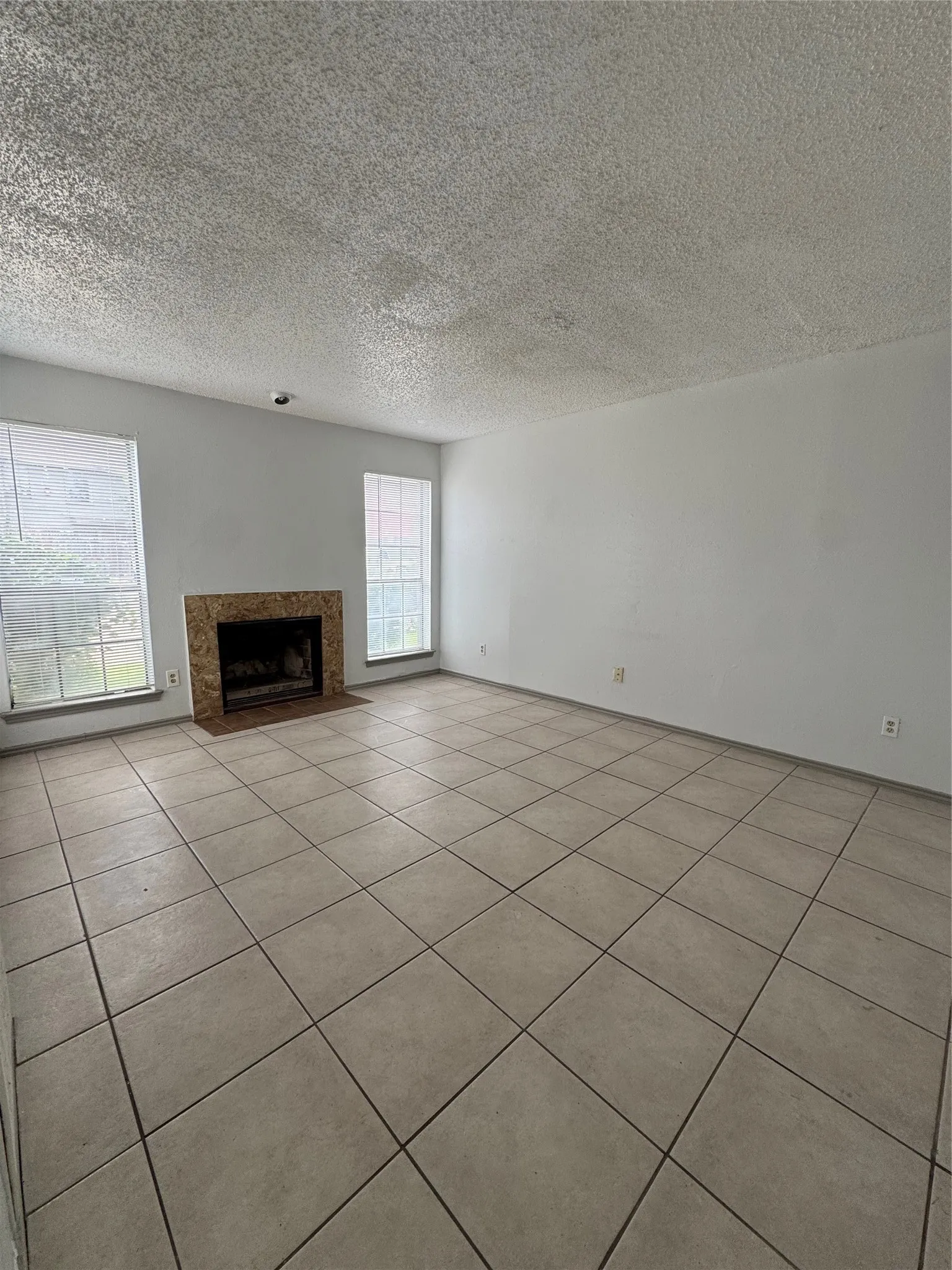 Spacious room featuring neutral tile flooring, a built-in fireplace with a stone surround, and multiple windows
