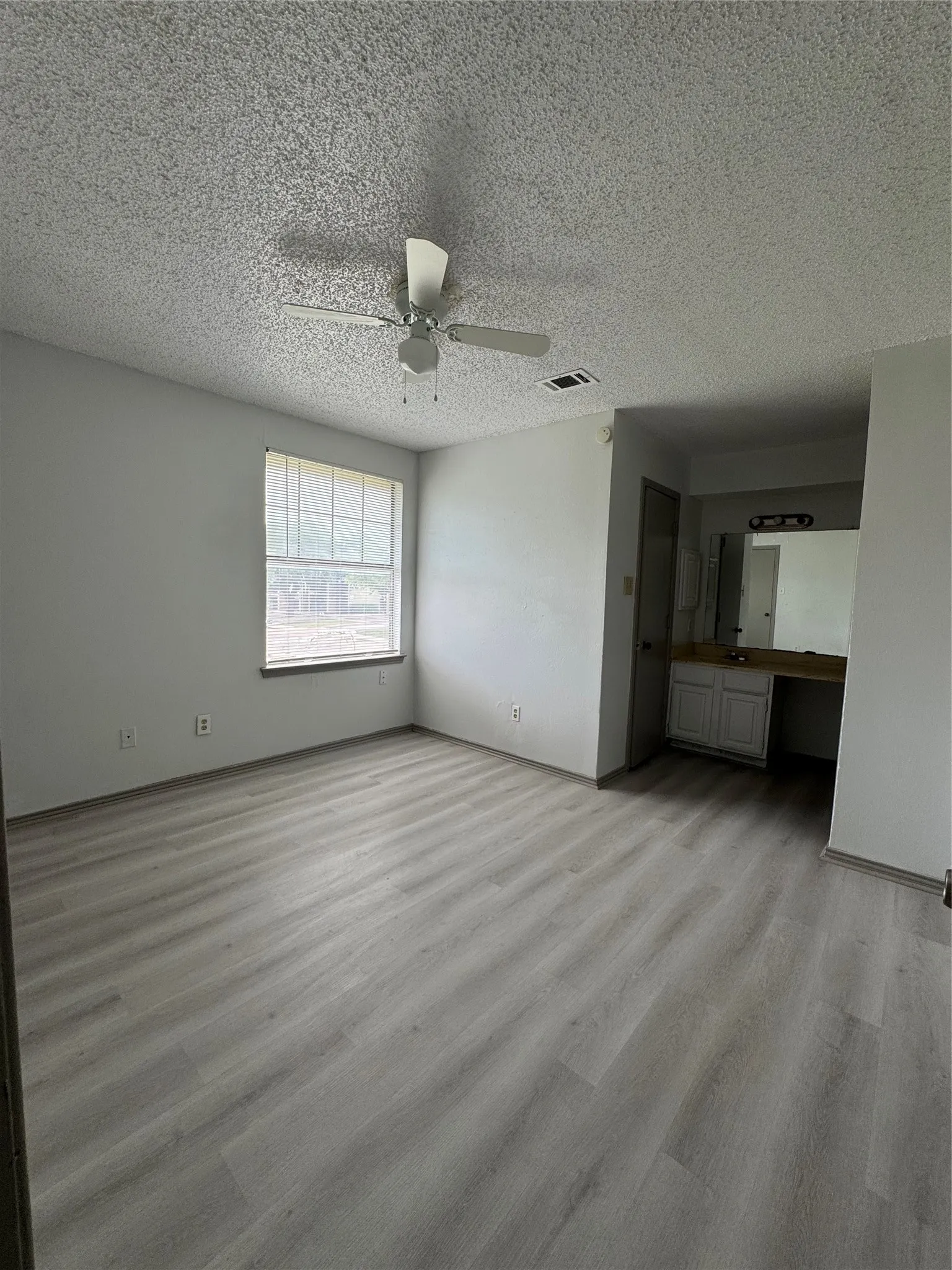Spacious room featuring light wood-finish flooring and a window with blinds