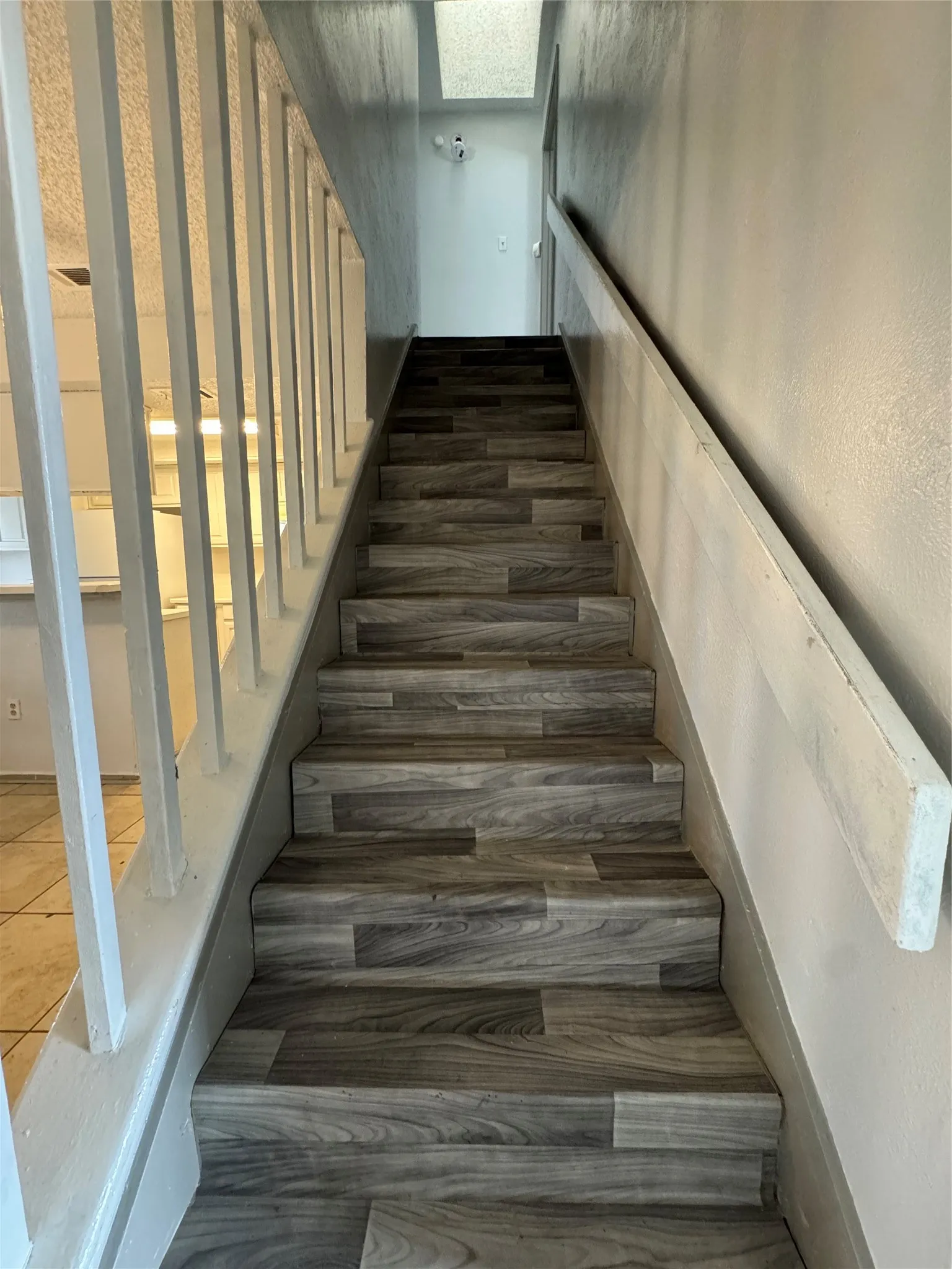 Staircase featuring wood-finish treads and risers, a painted handrail, and a contemporary skylight above