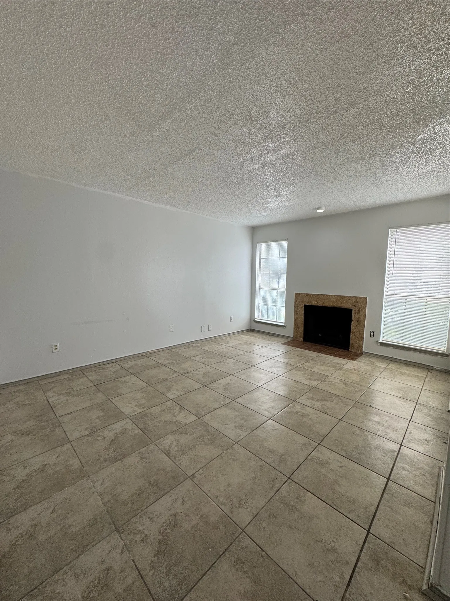 Spacious room featuring neutral tile flooring, a fireplace with a stone surround, and multiple windows for natural light