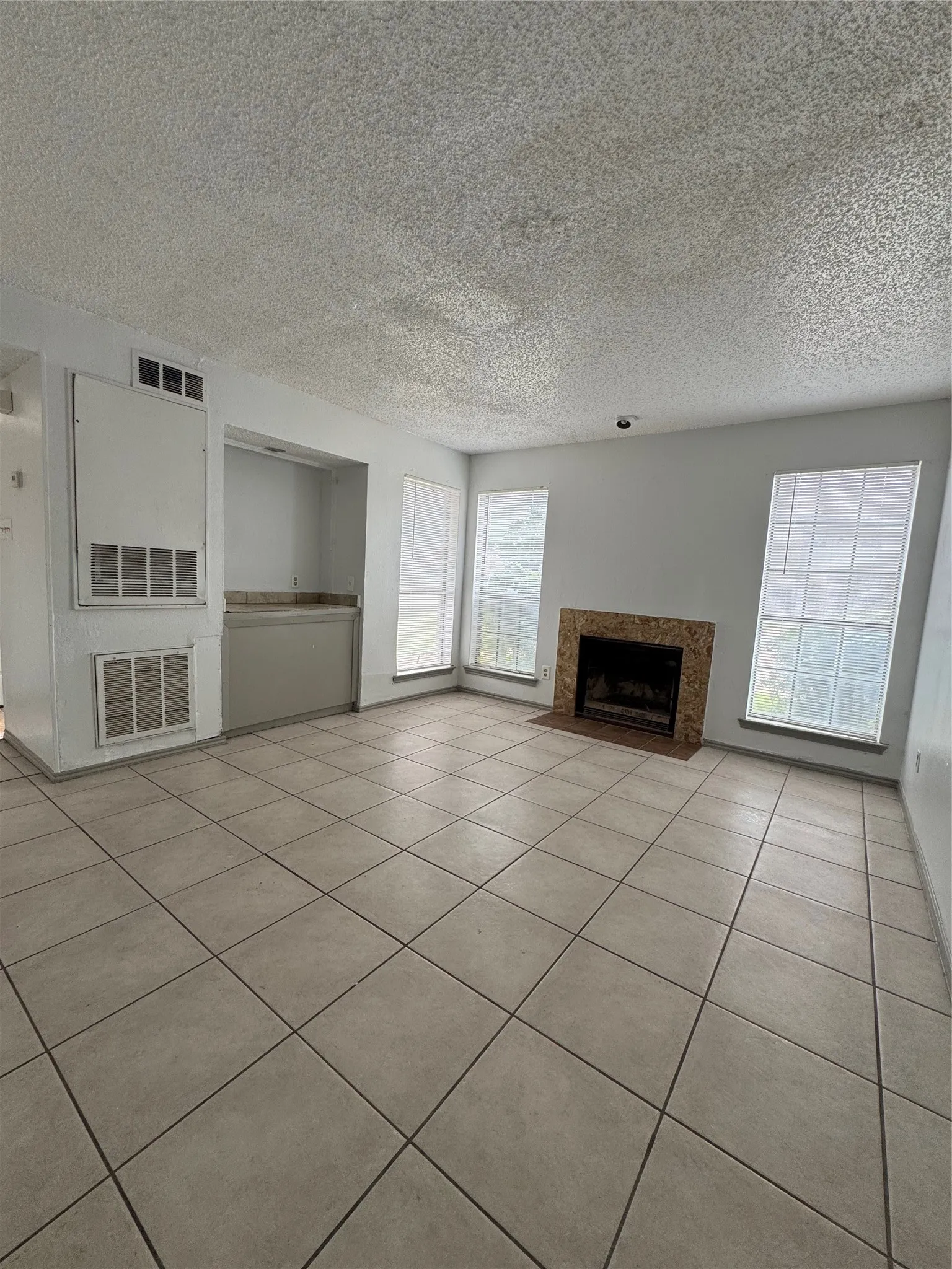 Spacious living area featuring diagonal tile flooring and a fireplace with a stone surround