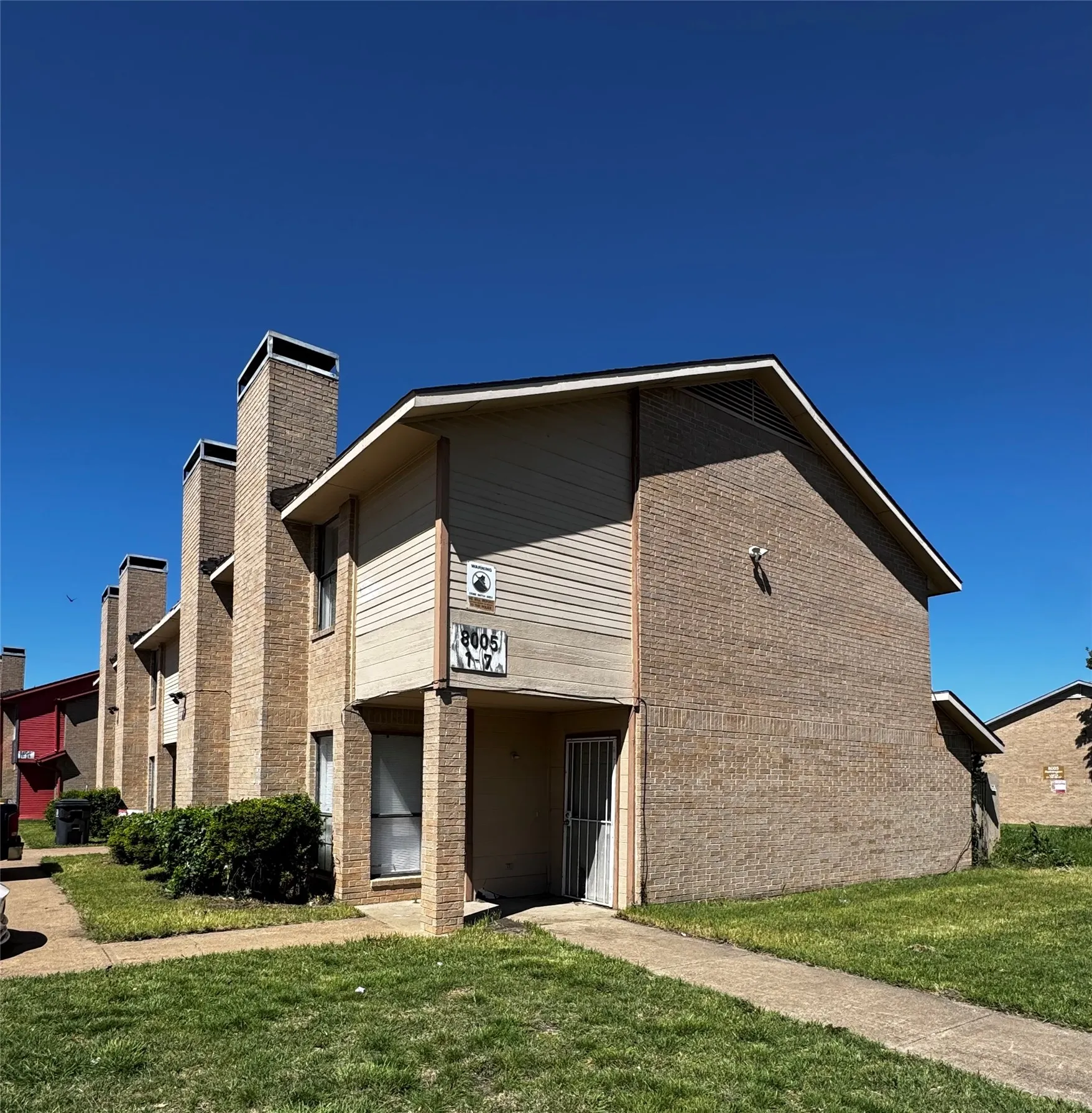 Brick exterior construction featuring multiple chimneys, a concrete walkway, and established green landscaping