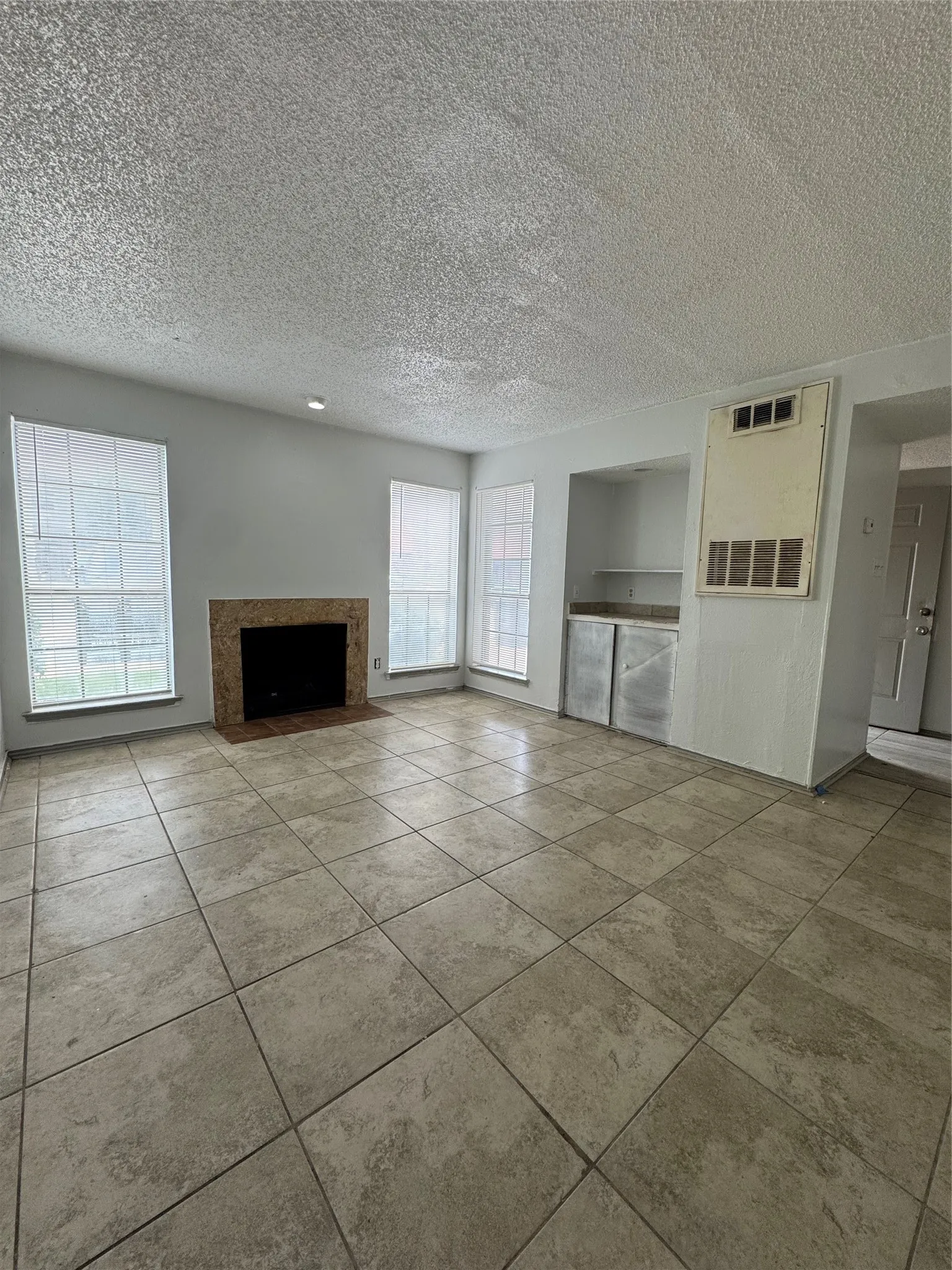 Spacious living area featuring large format tile flooring, a stone-surround fireplace, and multiple windows with blinds