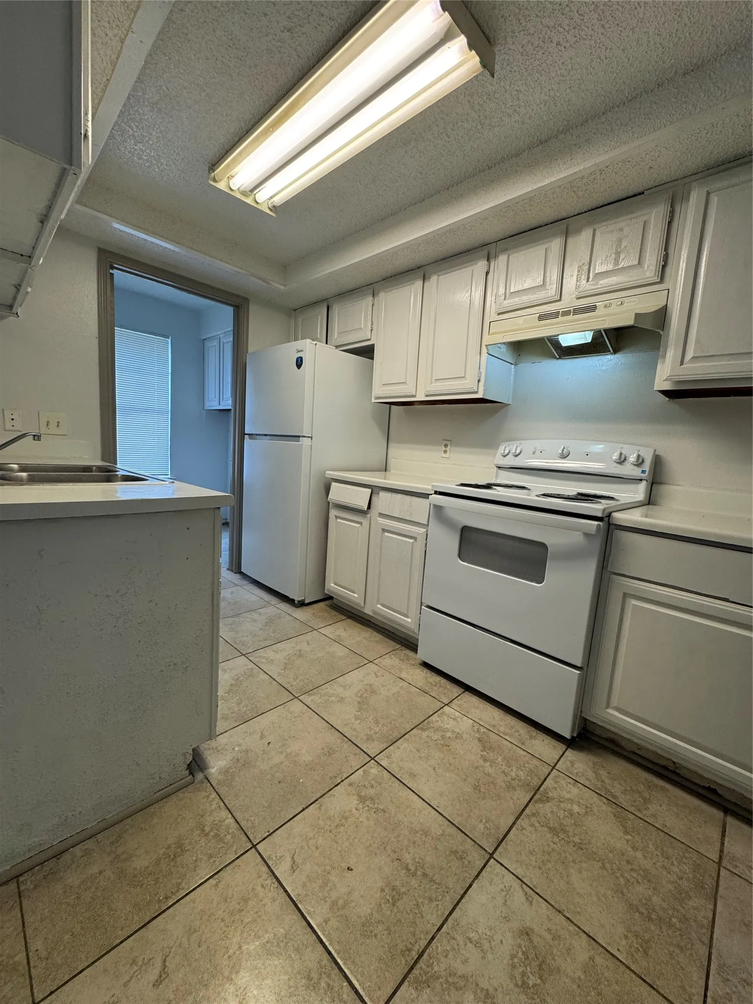 Kitchen featuring white cabinetry, a white refrigerator, a white electric range with an overhead microwave, tile flooring, and a luminous ceiling fixture