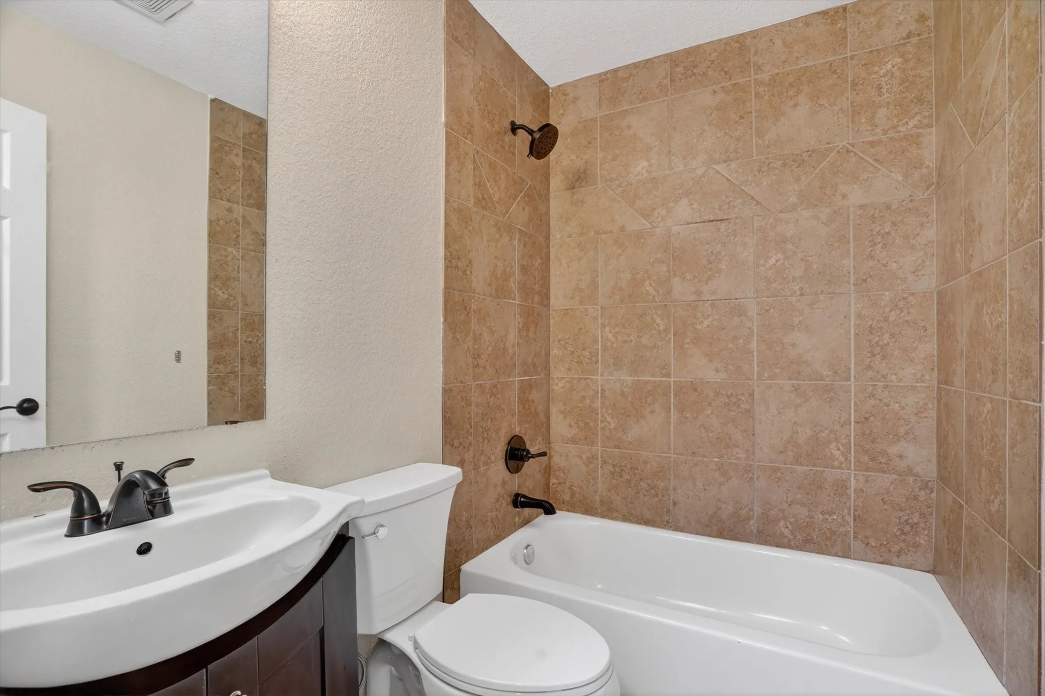 Bathroom featuring a white bathtub, ceramic tile shower surround with decorative accents, a white toilet, and a vanity with a white basin sink and dark-finish cabinetry
