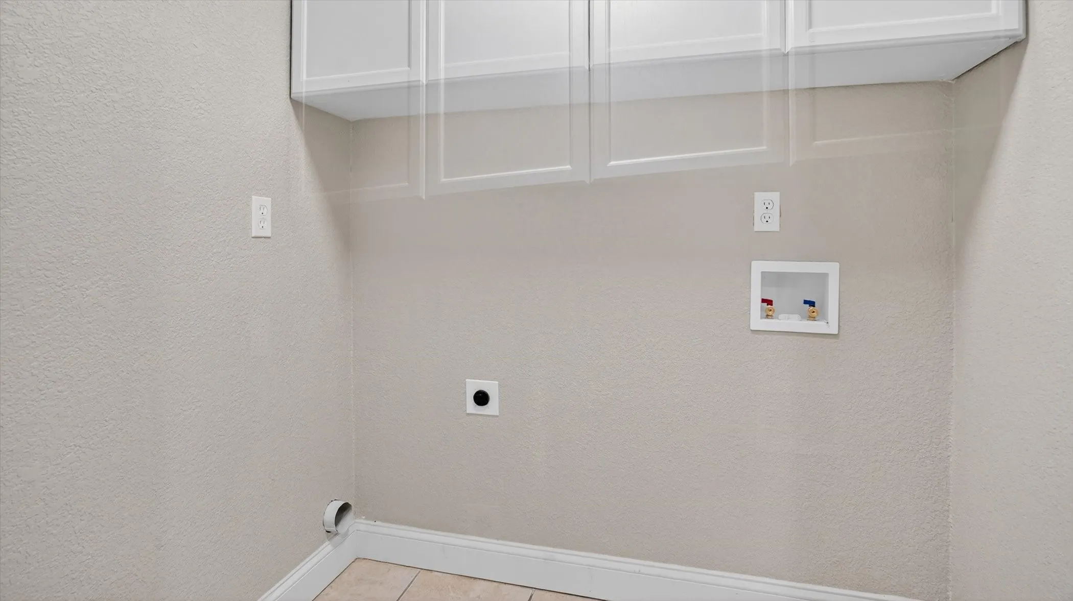 Laundry area featuring tile flooring, white shaker-style cabinetry, and dedicated hookups for appliances