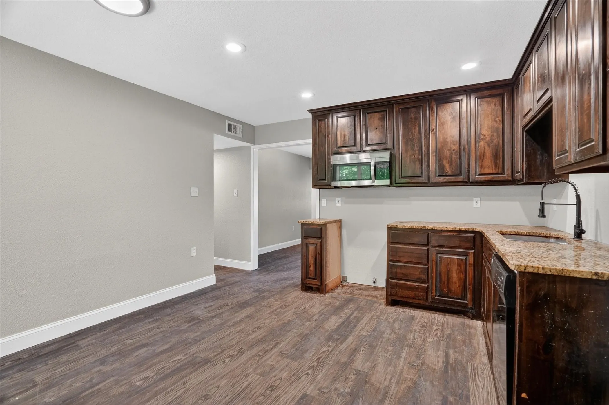 Kitchen featuring wood-finish flooring, dark wood cabinetry, granite-style countertops, an undermount sink with a gooseneck faucet, and a stainless steel microwave