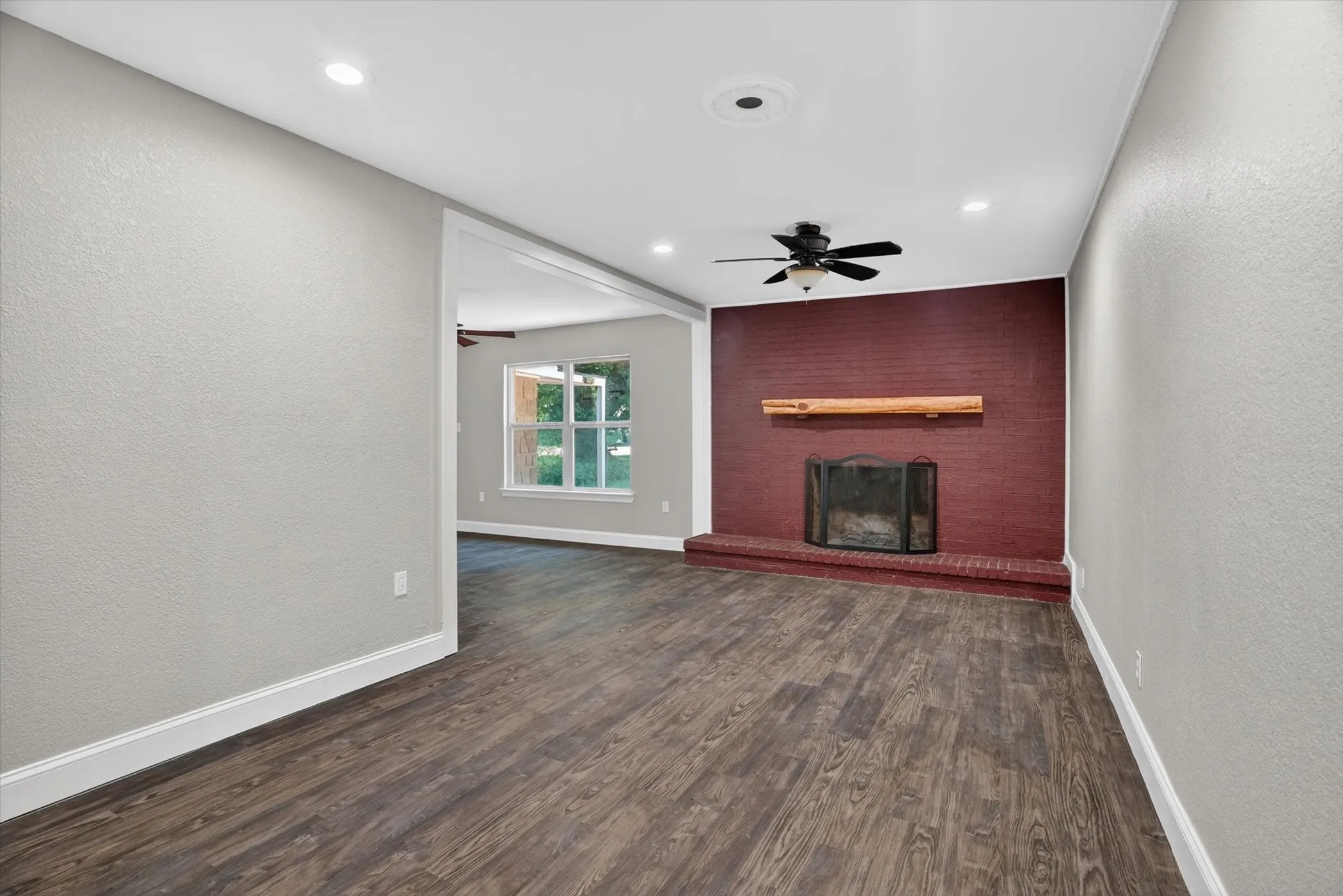 Spacious room featuring wood-finish flooring, a red brick fireplace with a natural wood mantel, recessed lighting, and a ceiling fan