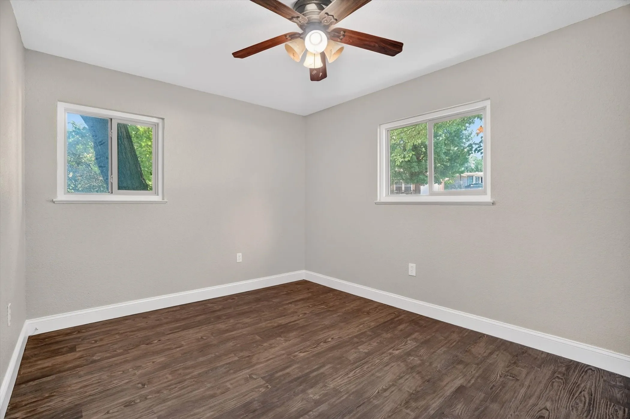 Room featuring wood-finish flooring, two windows with white trim, light gray wall paint, and a ceiling fan with light fixture