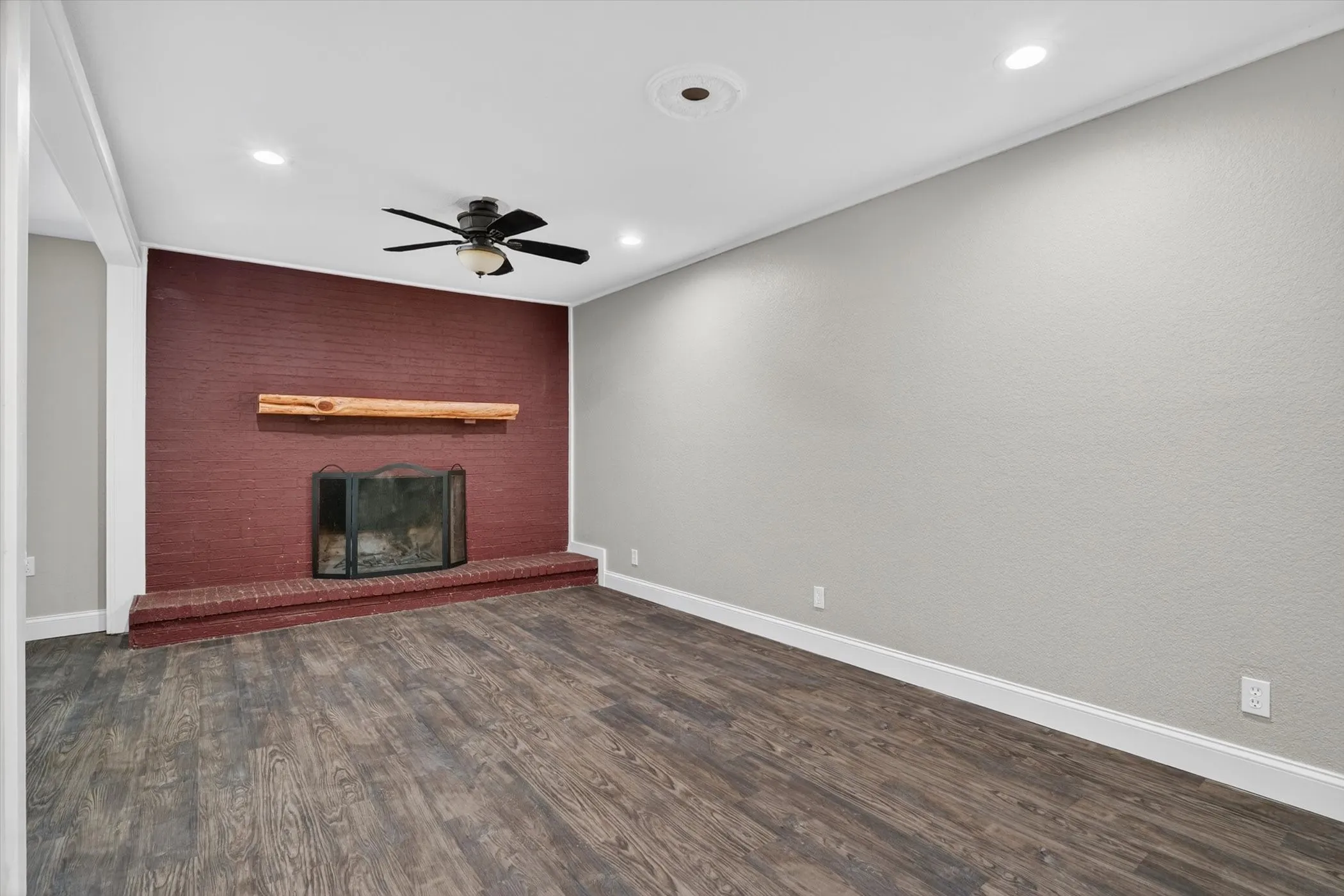 Spacious room featuring a red brick fireplace with a wood mantle, wood-finish flooring, a ceiling fan, and recessed lighting
