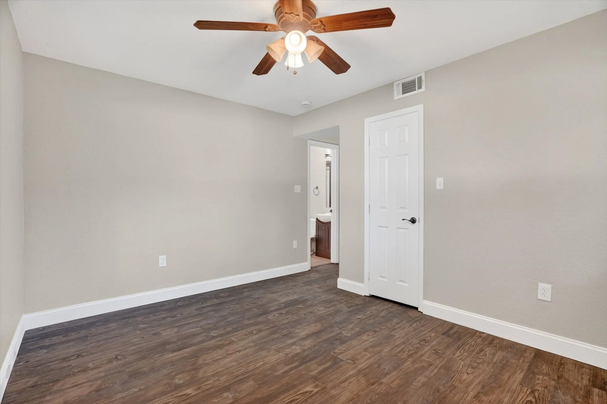 Spacious interior room featuring wood-finish flooring, light neutral wall paint, and white baseboards