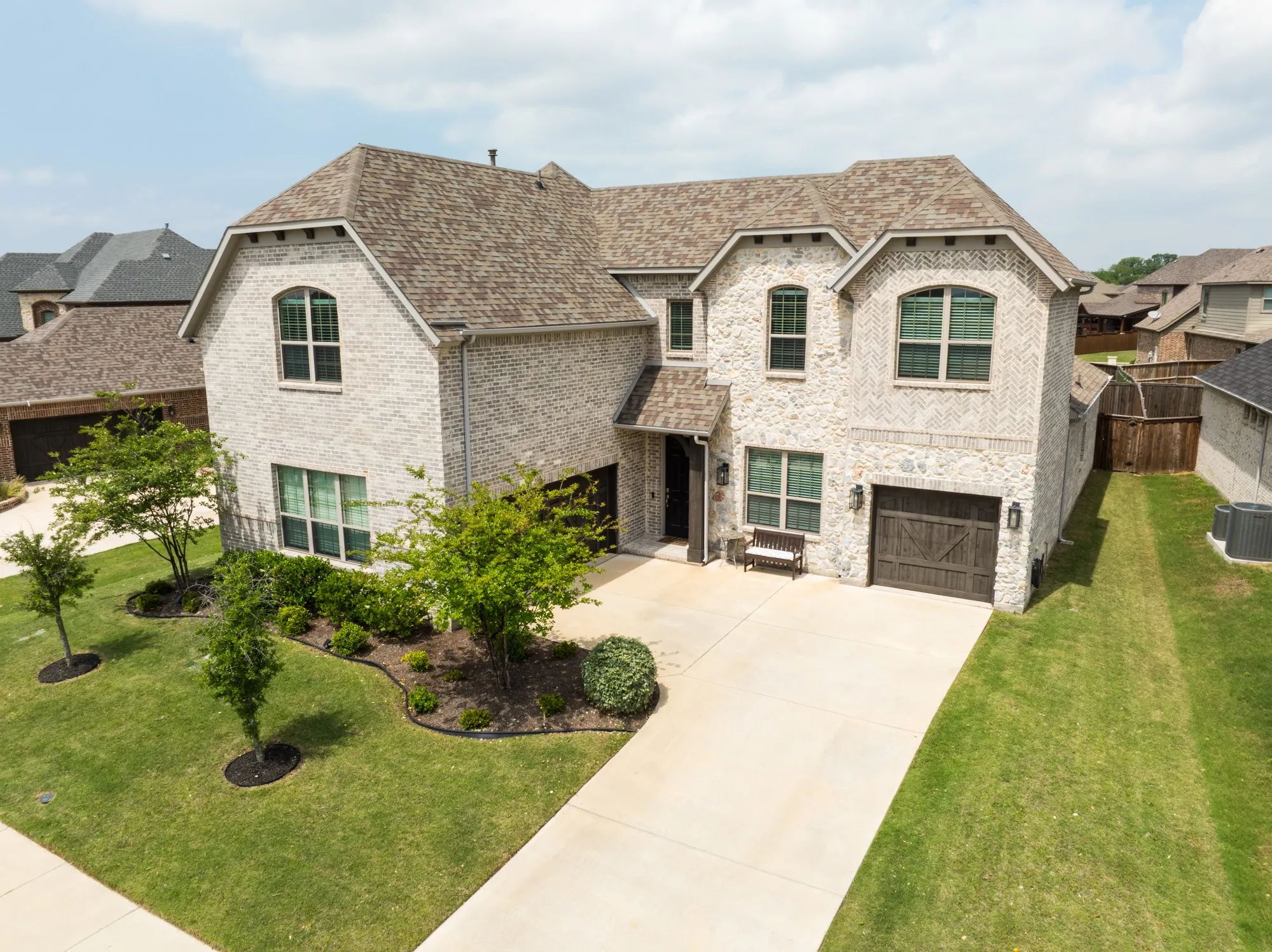 Front featuring 3 split car garage, landscaping and light colored brick.