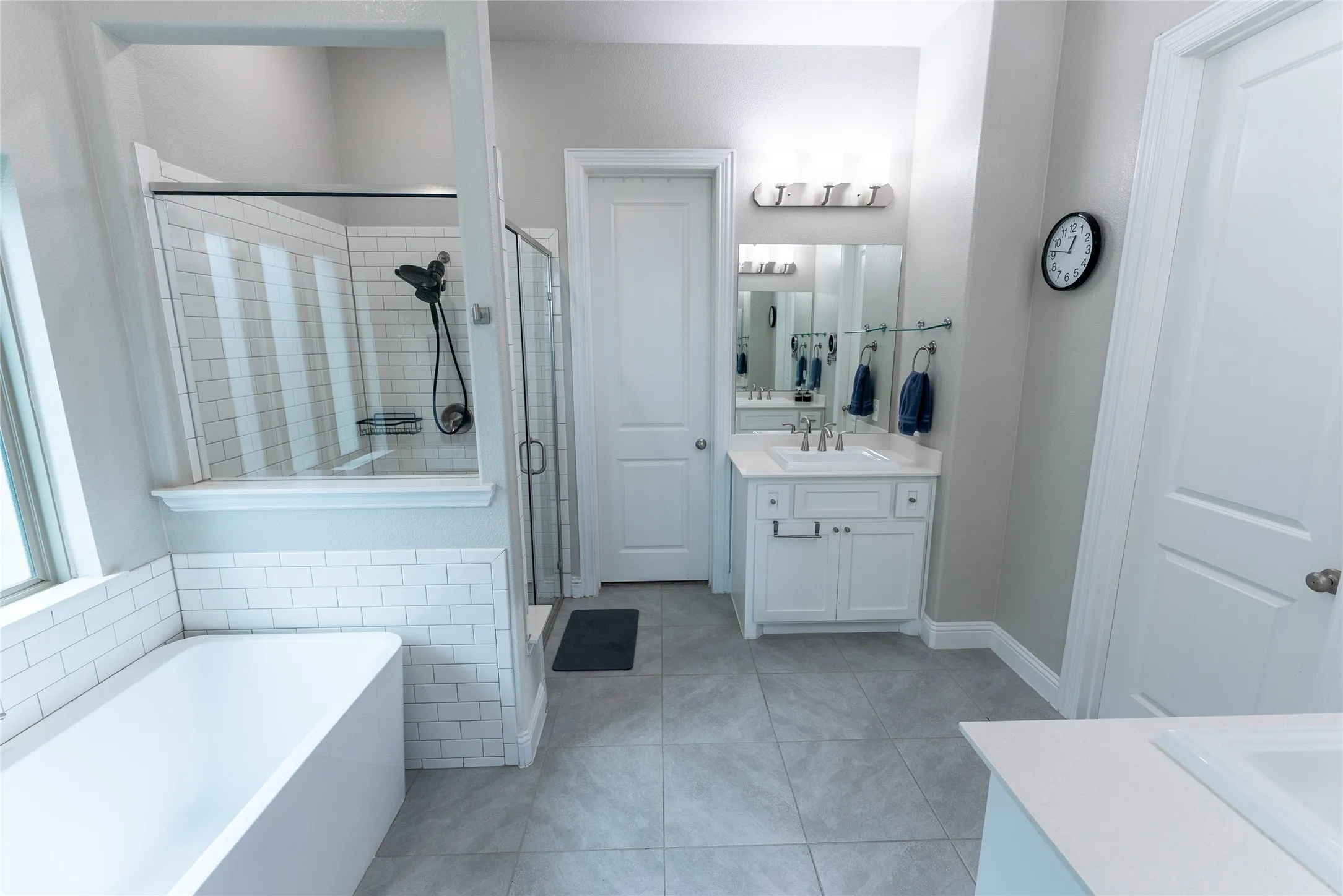 Primary bathroom featuring a free standing tub, separate shower, separate vanities, walk in closet and tile floors.