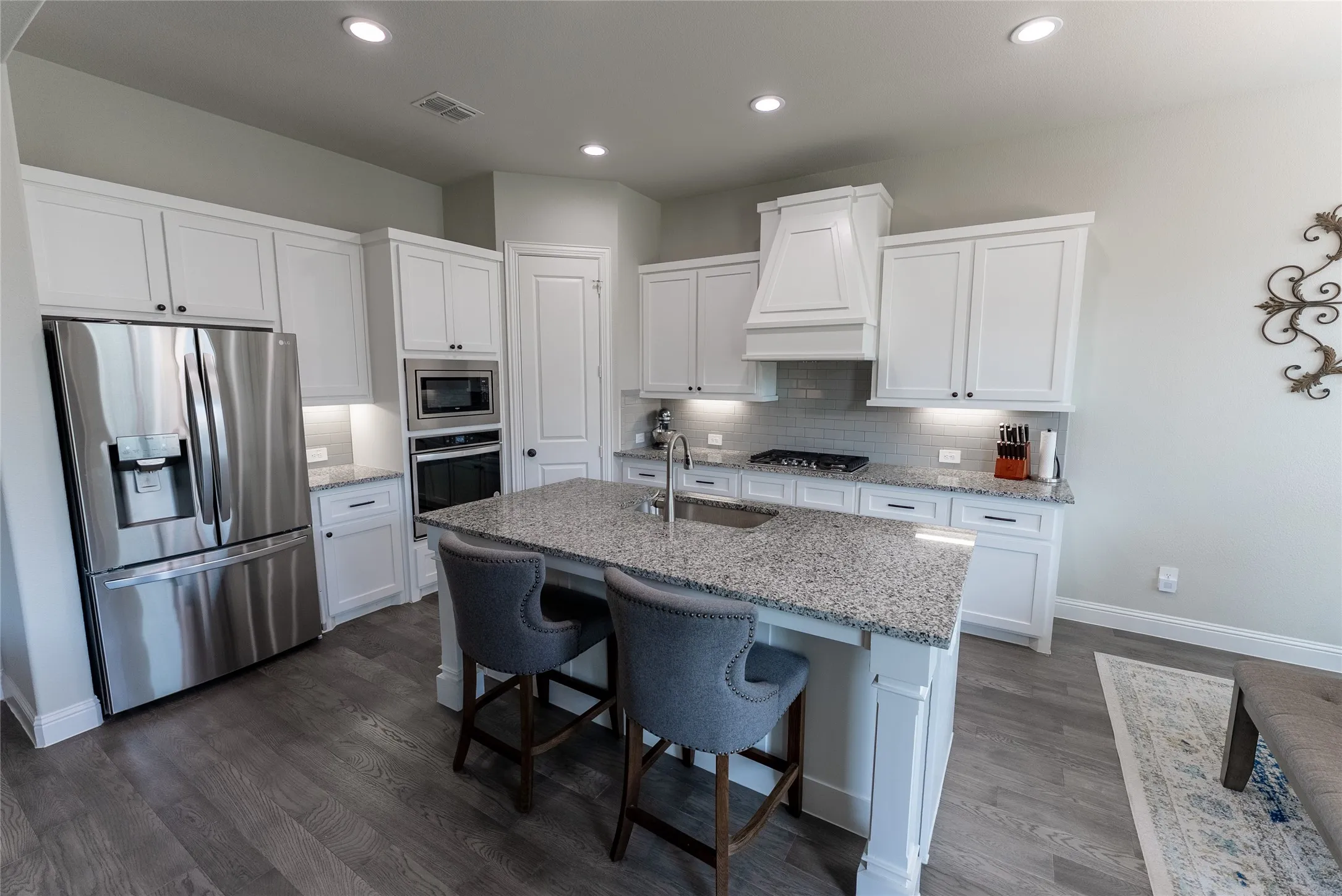 Kitchen with LVP flooring, granite countertops, gas stove, hood, and built-in microwave and oven.