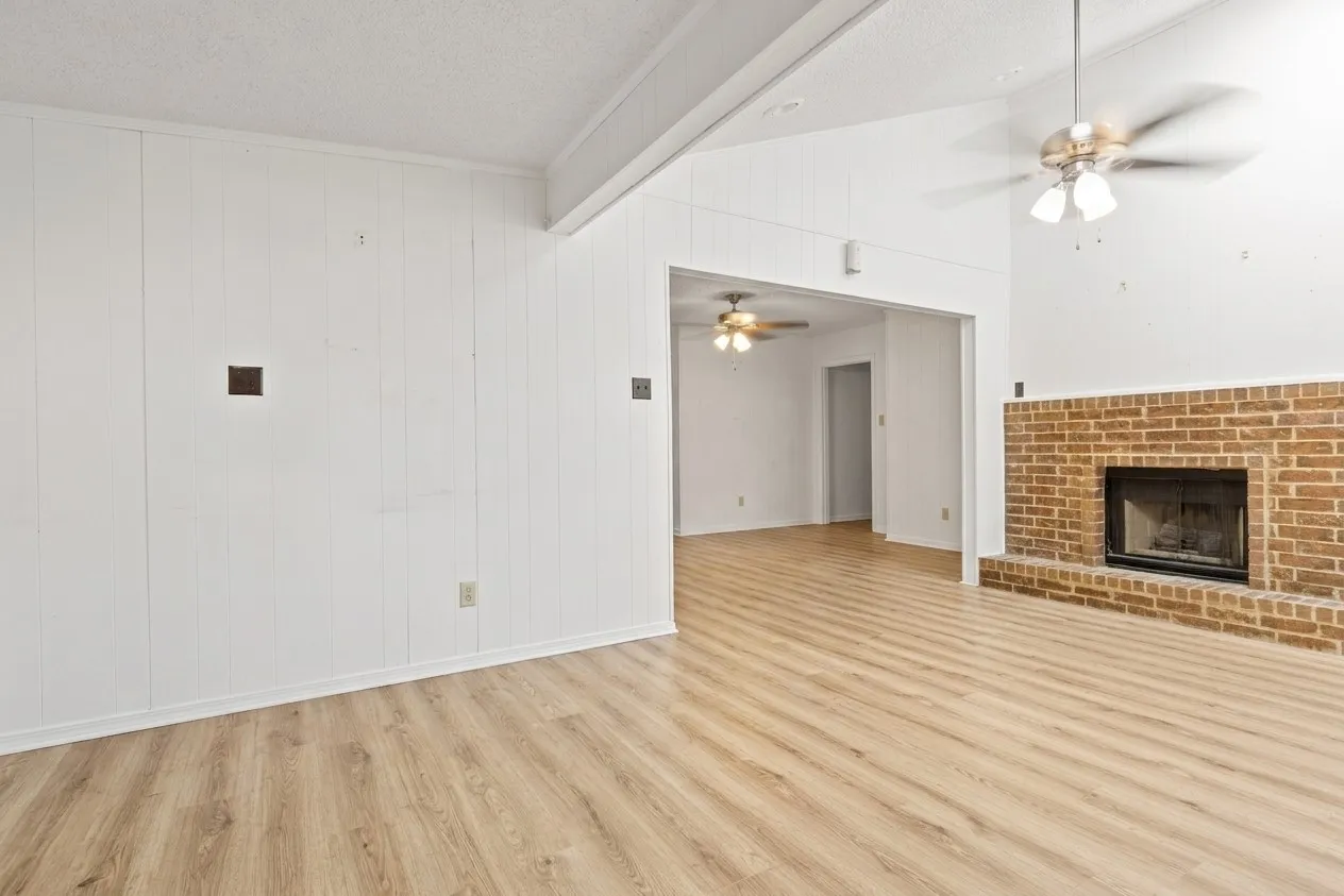 Virtually Staged Vaulted ceiling den (Empty)  featuring wood-finish flooring, a brick fireplace, and white paneling
