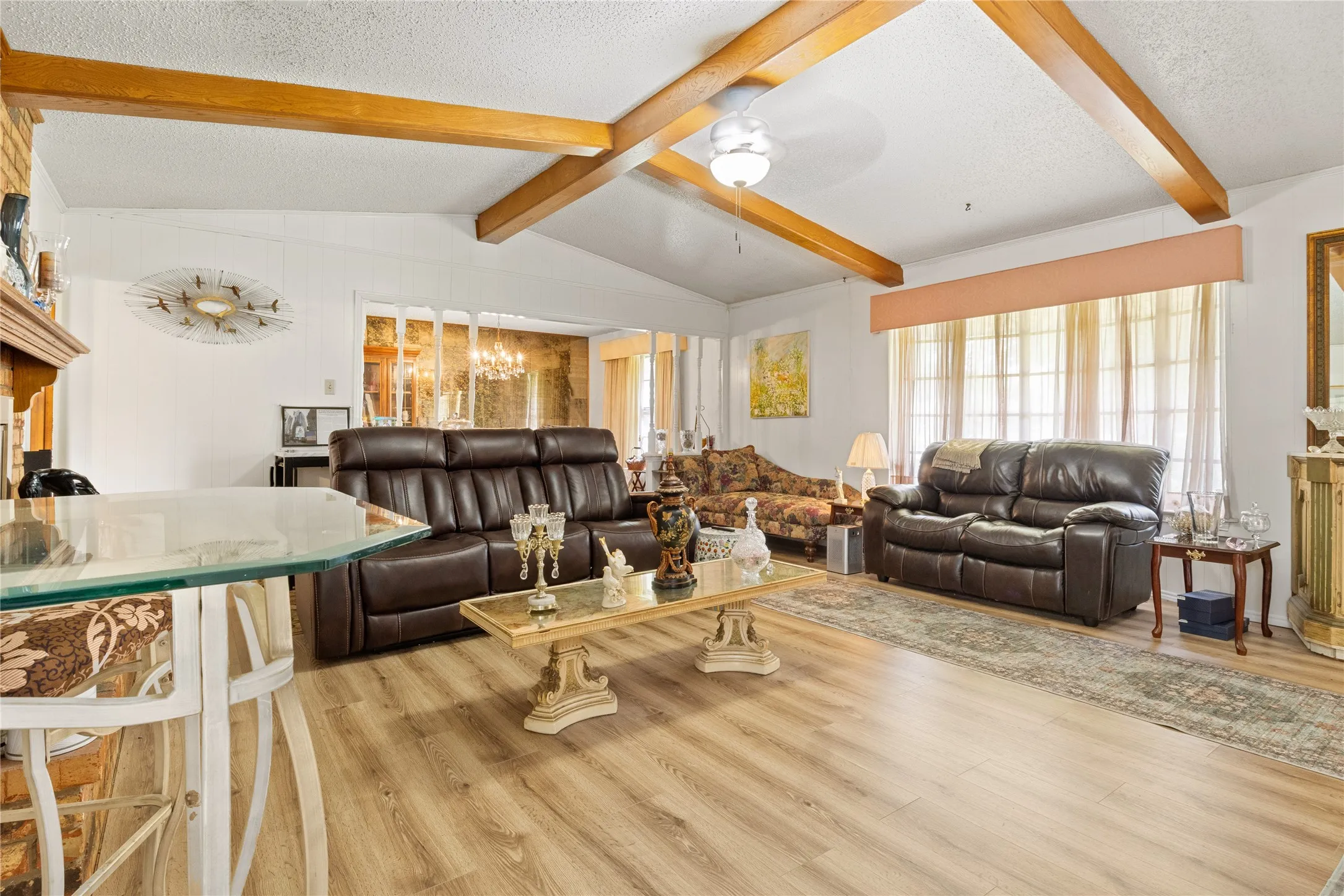 Living area featuring wood-finish flooring, exposed ceiling beams, and a fireplace with a brick surround