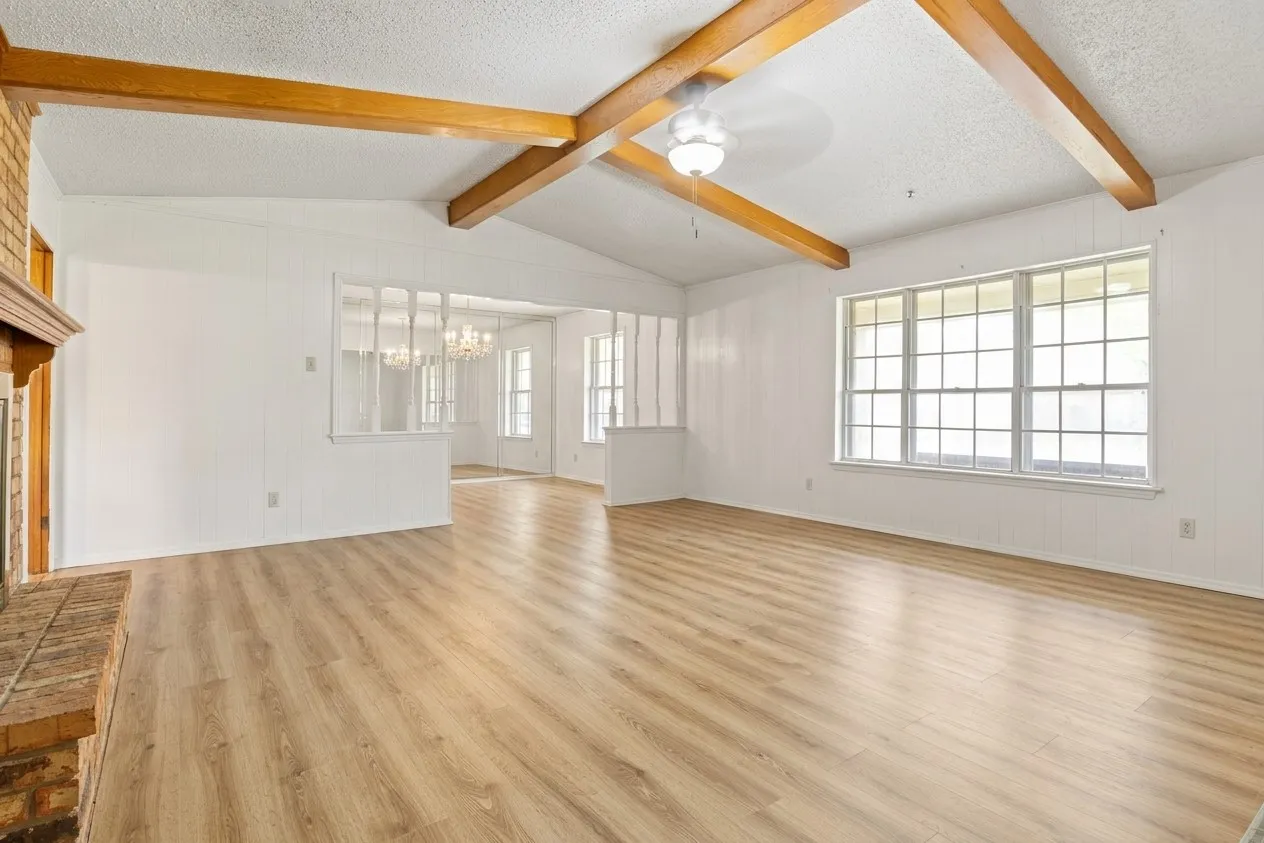 Virtually Staged (Empty) - Living area featuring wood-finish flooring, exposed ceiling beams, and a fireplace with a brick surround