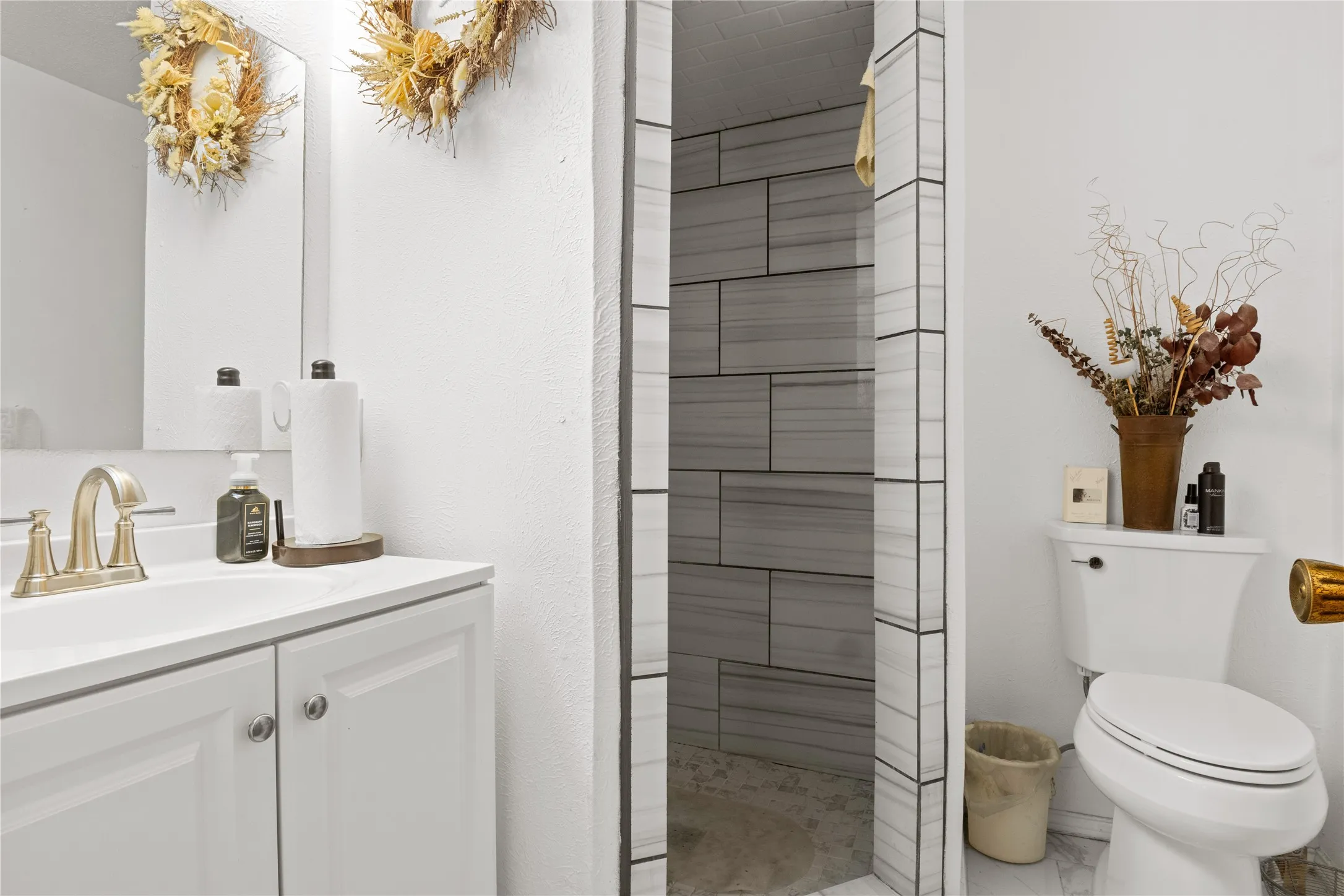 Primary Bathroom featuring a newly tiled shower w/ white vanity and an integrated sink, brushed nickel faucet, and paneled cabinetry