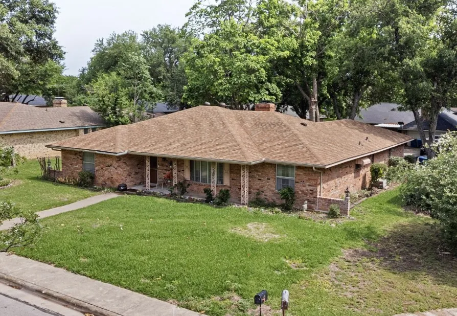 Traditional Beautiful Brick Home featuring a new brown shingle roof, mature tree canopy, and an expansive front lawn