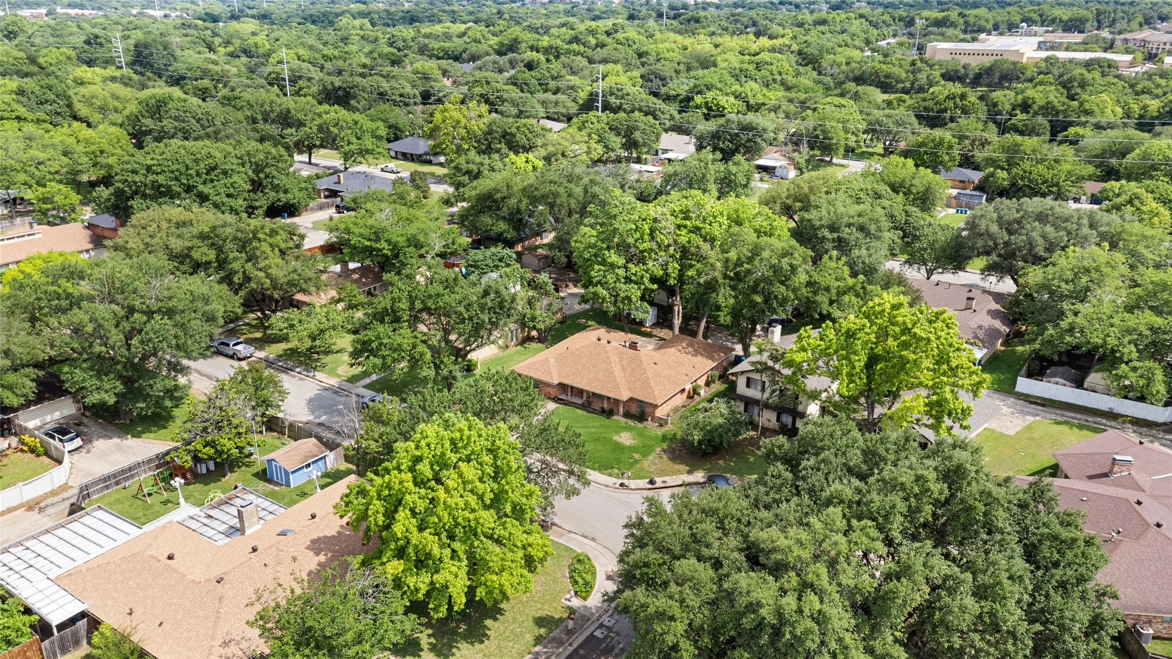 Expansive aerial perspective showcasing a residential area with abundant mature trees and a traditional brick home with a brown shingle roof