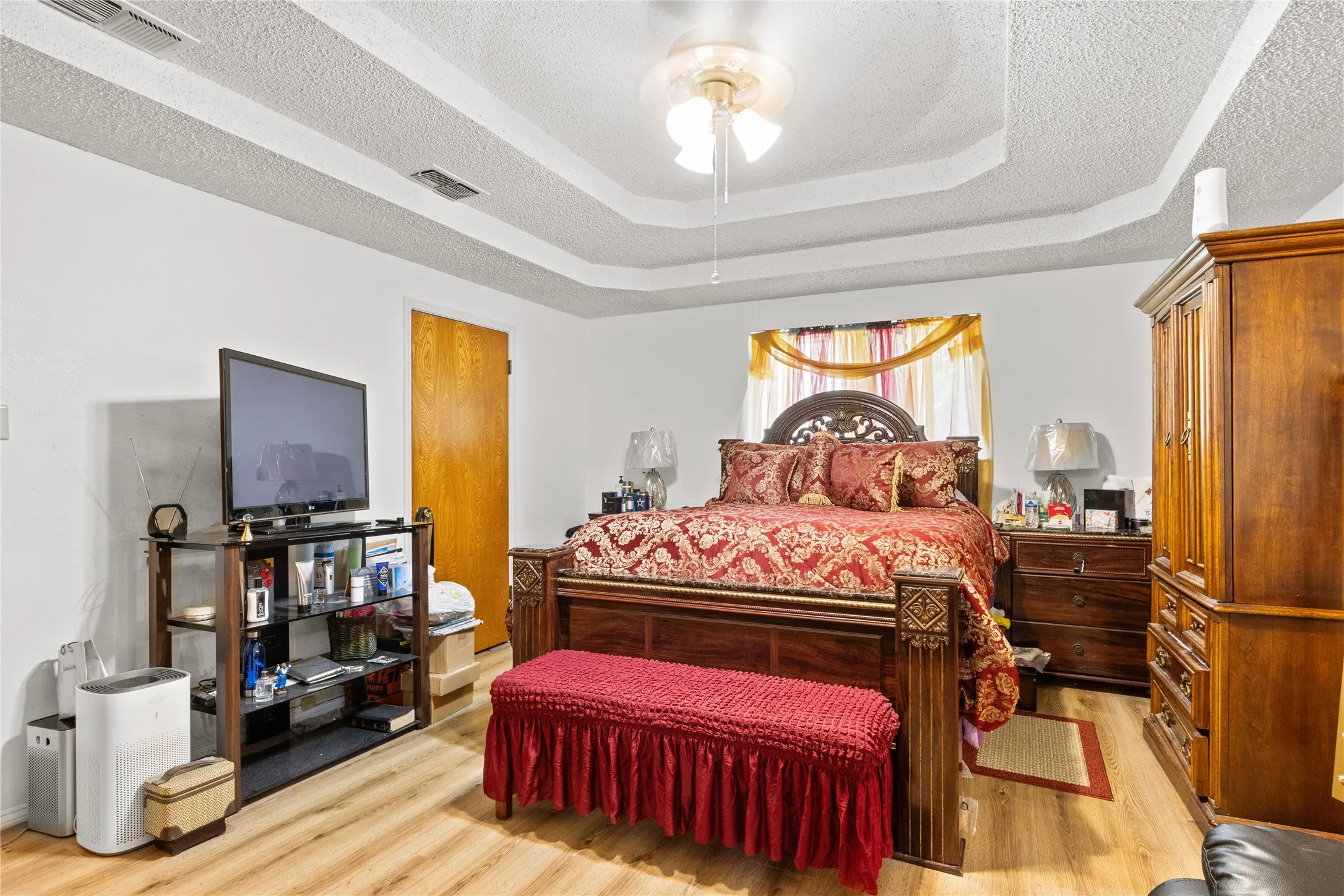 Spacious Primary Bedroom featuring wood-finish flooring, a recessed tray ceiling, and a ceiling fan