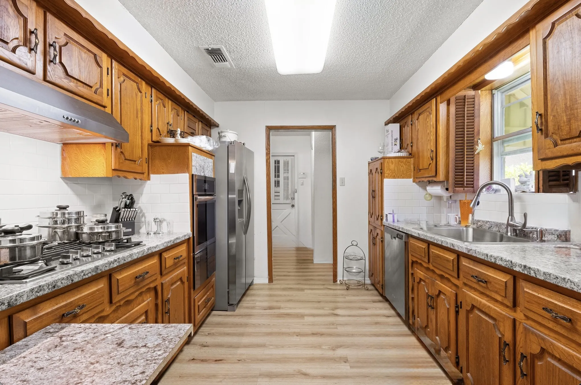 Galley kitchen featuring wood cabinetry, light-toned wood-finish flooring, and white subway tile backsplash