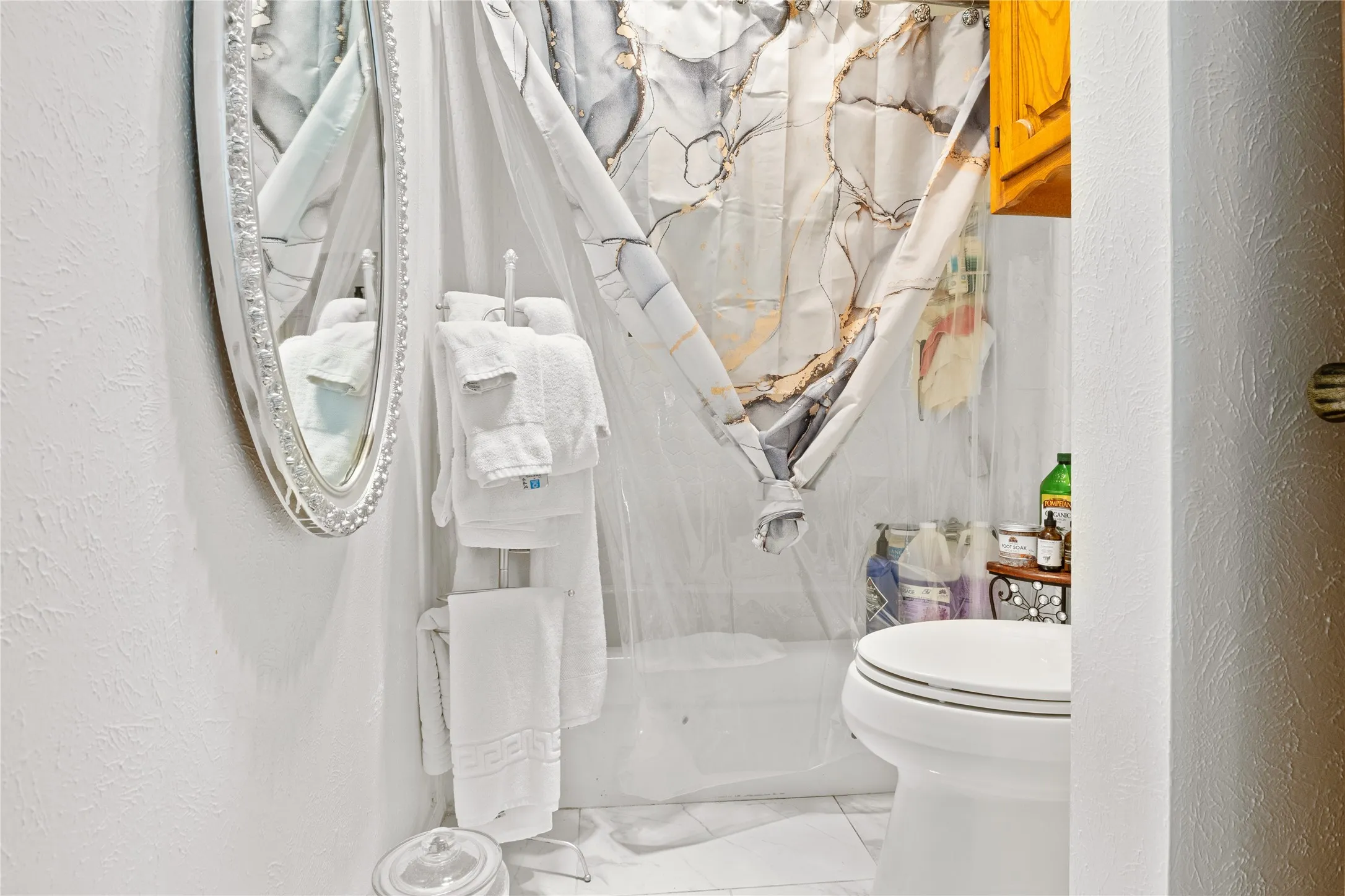 Bathroom featuring a white bathtub, ceramic tile flooring, a white toilet, and a decorative oval mirror with an ornate frame