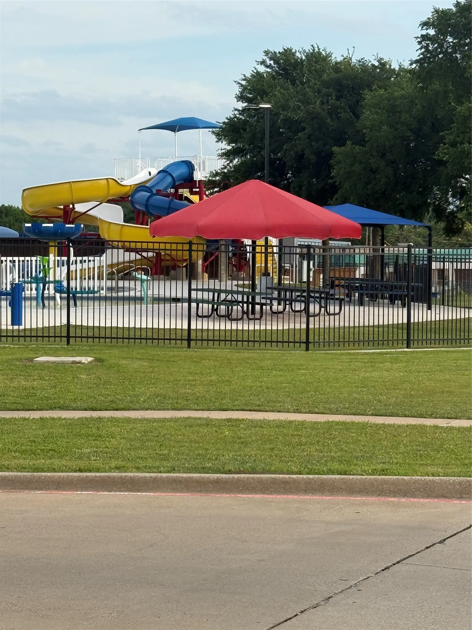 Community aquatic center featuring multiple water slides, shaded picnic tables, and a fenced perimeter