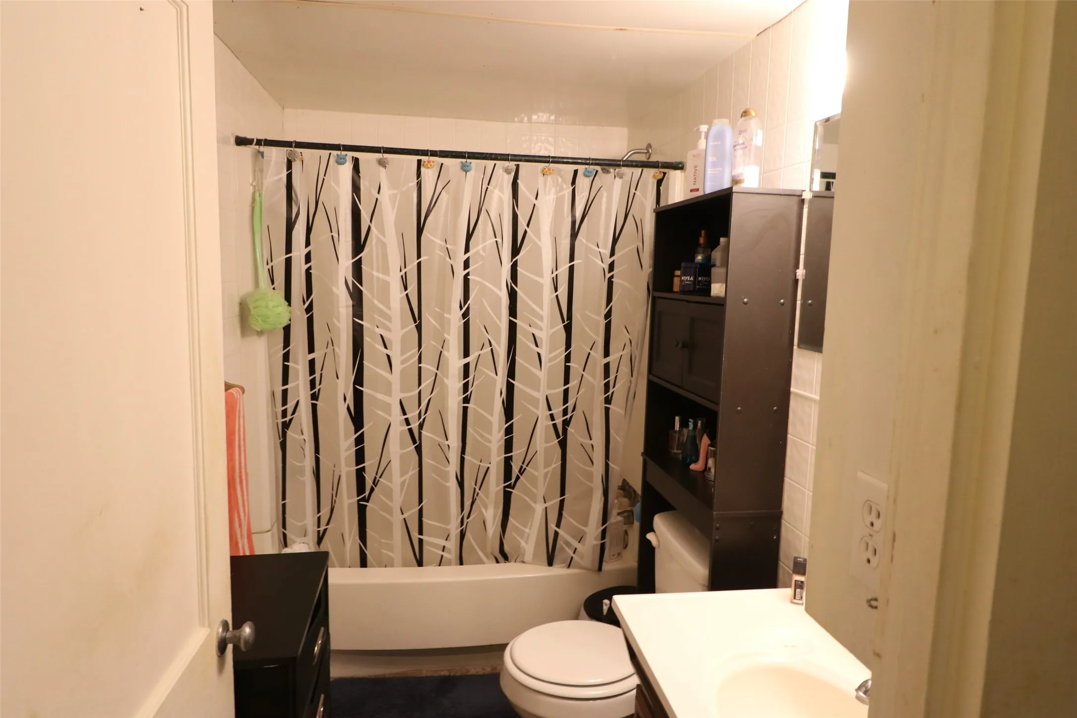 White tiled shower surround with bathtub and a dark wood-finish storage tower