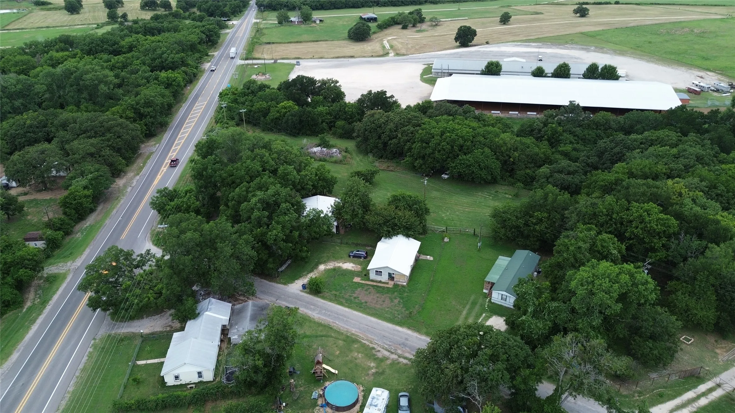 Expansive rural property featuring multiple residential structures, mature trees, and a substantial outbuilding with a light-colored roof