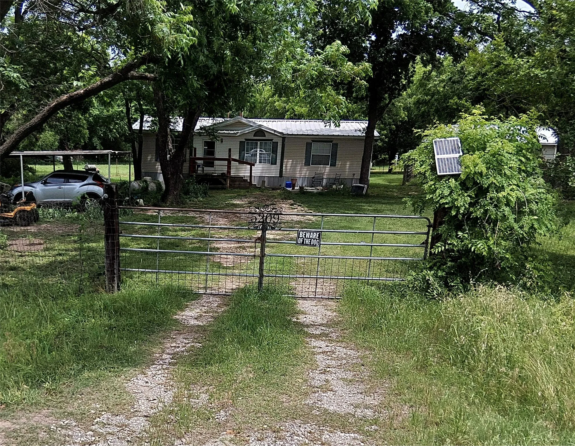 Gated gravel driveway leading to a residence set amidst mature trees