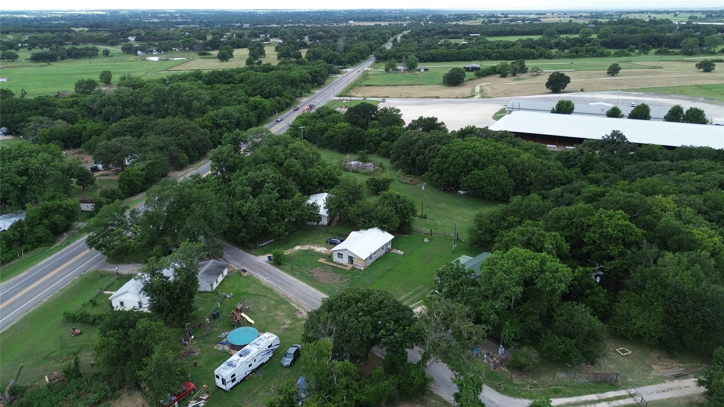 Rural setting featuring multiple residences, mature trees, and paved roadways