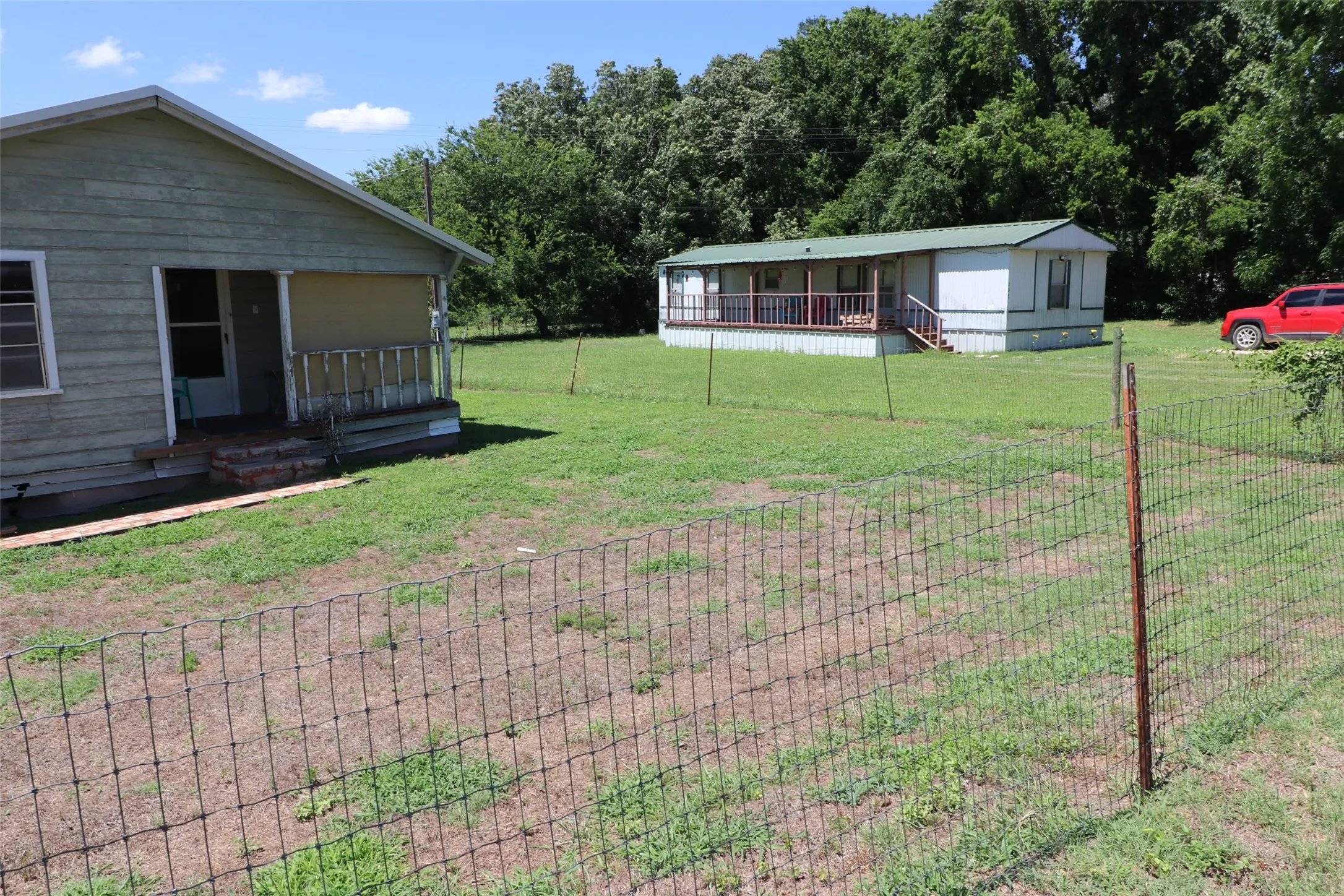 Grassy expanse featuring two distinct residential structures and mature perimeter trees