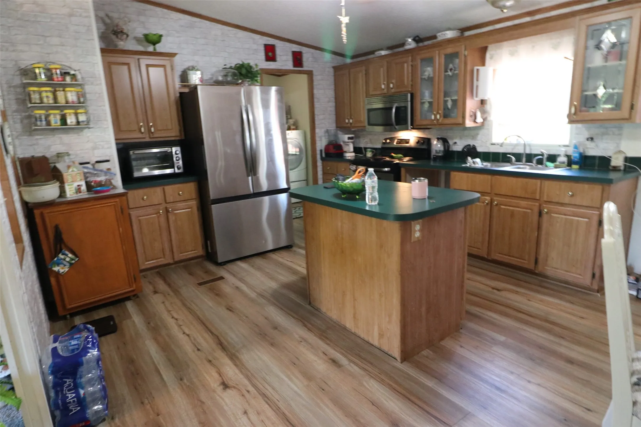 Kitchen featuring wood-finish flooring, a central island with a solid surface countertop, wood cabinetry, a stainless steel refrigerator, and a built-in microwave