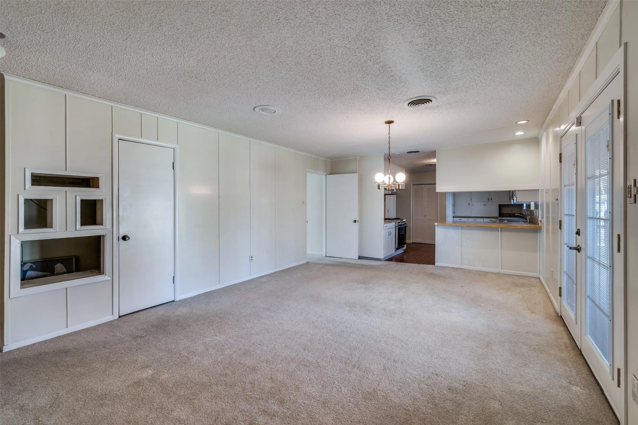 Spacious room with light-toned carpet flooring, built-in shelving, white paneled walls, and French doors
