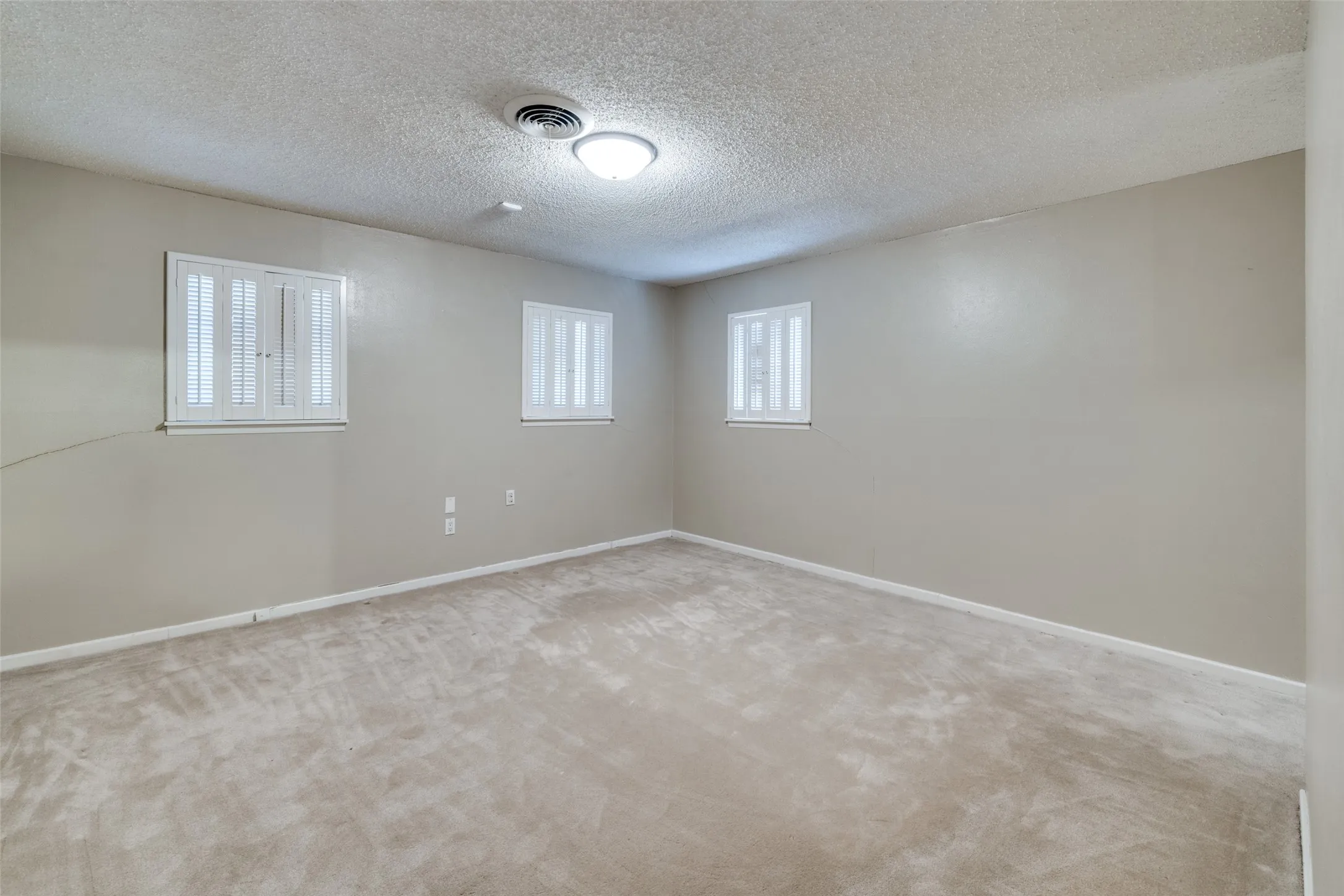 Carpeted interior space featuring neutral wall paint, two windows with white plantation shutters, and a ceiling-mounted light fixture