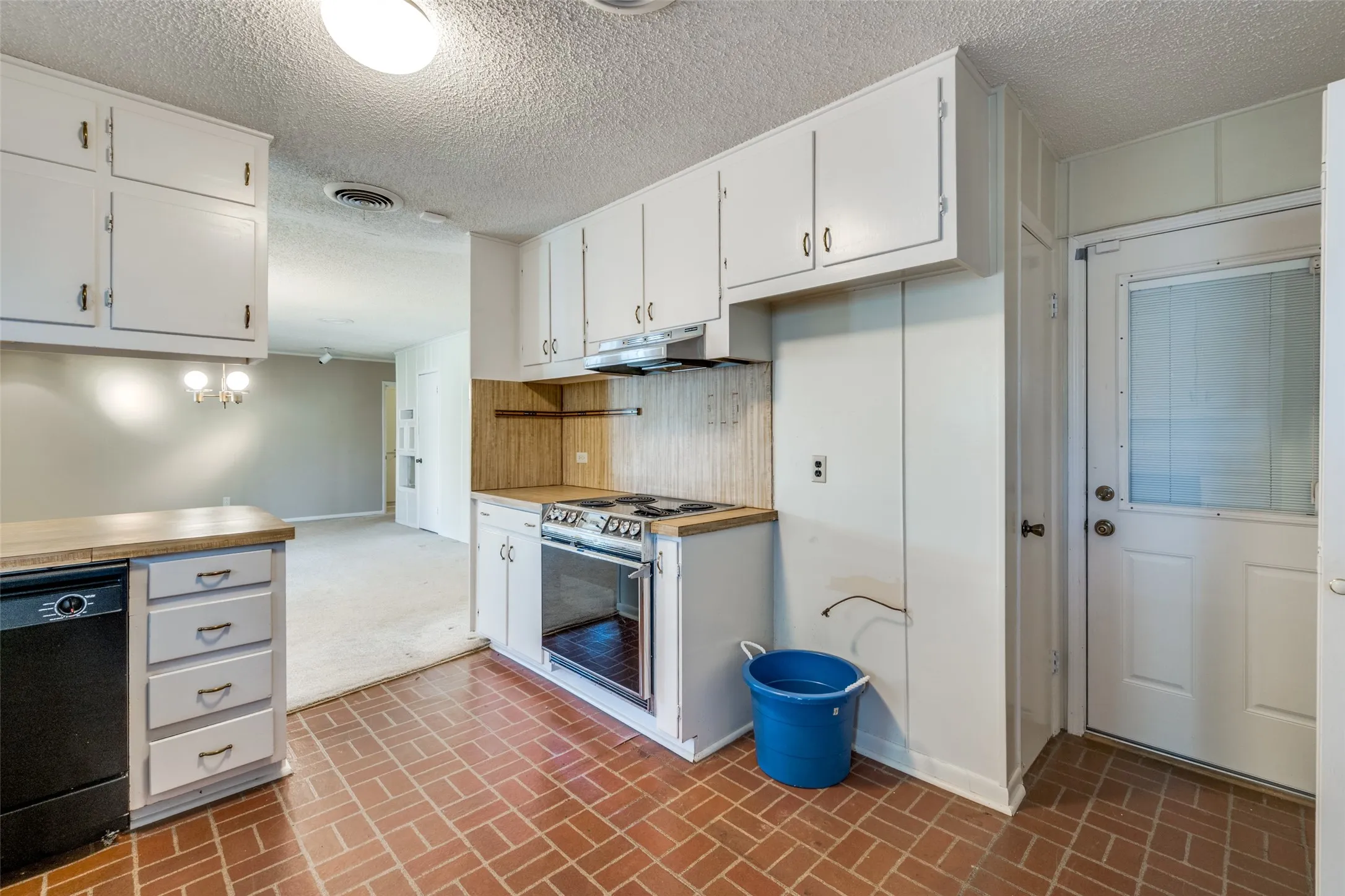 Kitchen featuring brick-patterned flooring, white cabinetry, wood-finish countertops, a built-in oven with electric cooktop, and a glass-paned exterior door