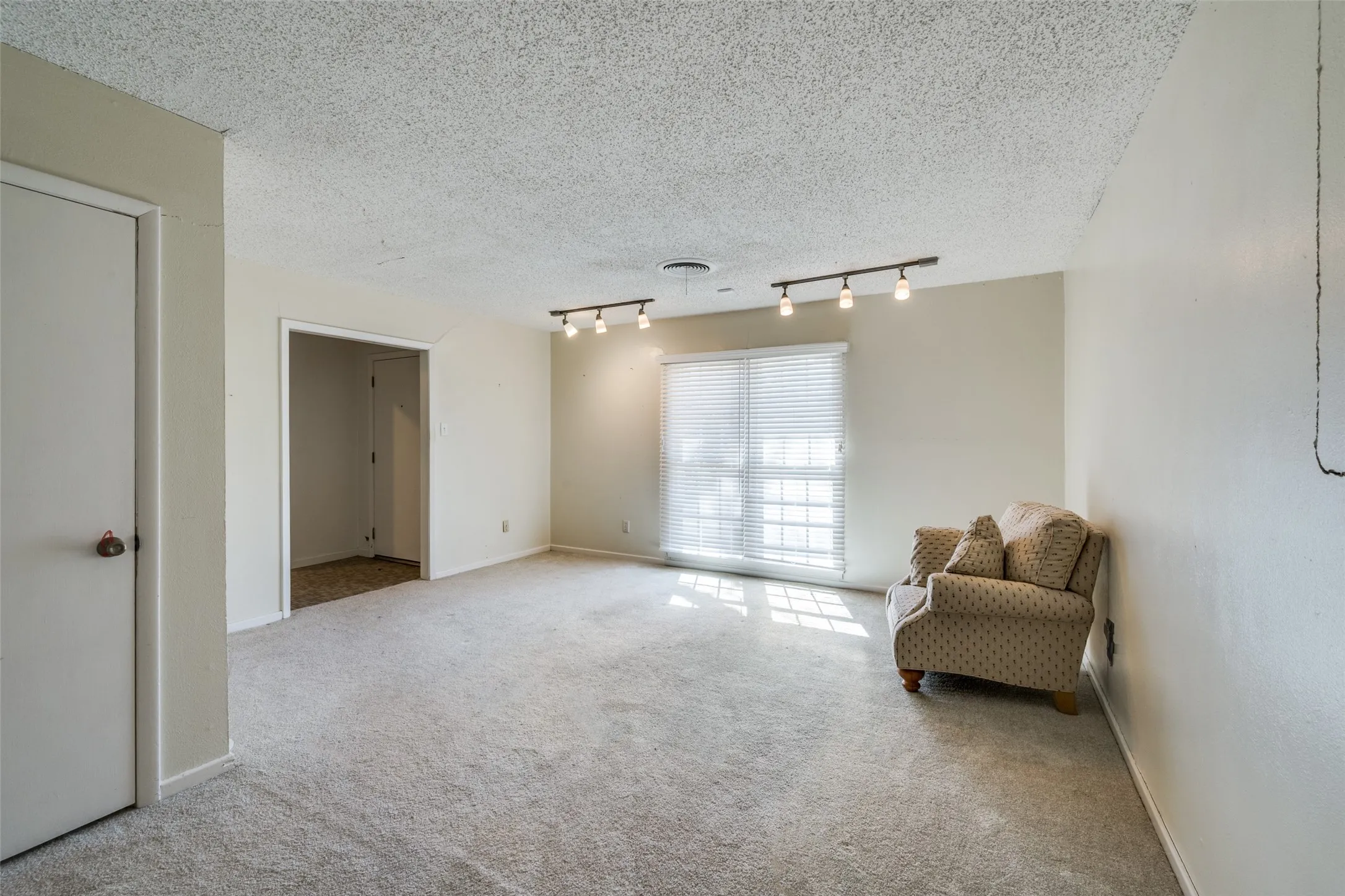 Carpeted interior space featuring track lighting, a window with horizontal blinds, and neutral wall paint