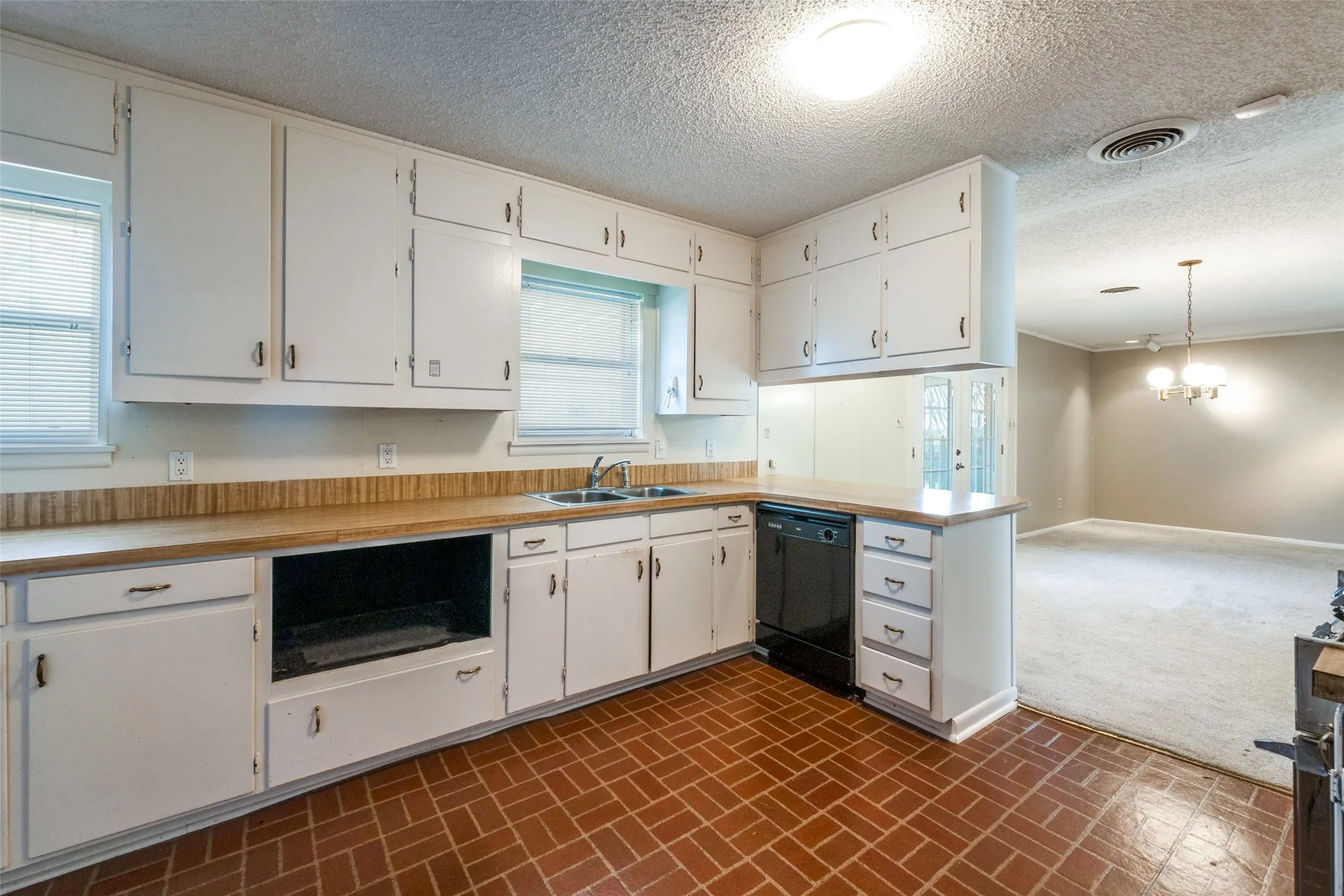 Kitchen featuring white cabinetry, brick-patterned flooring, laminate countertops, and a black built-in dishwasher