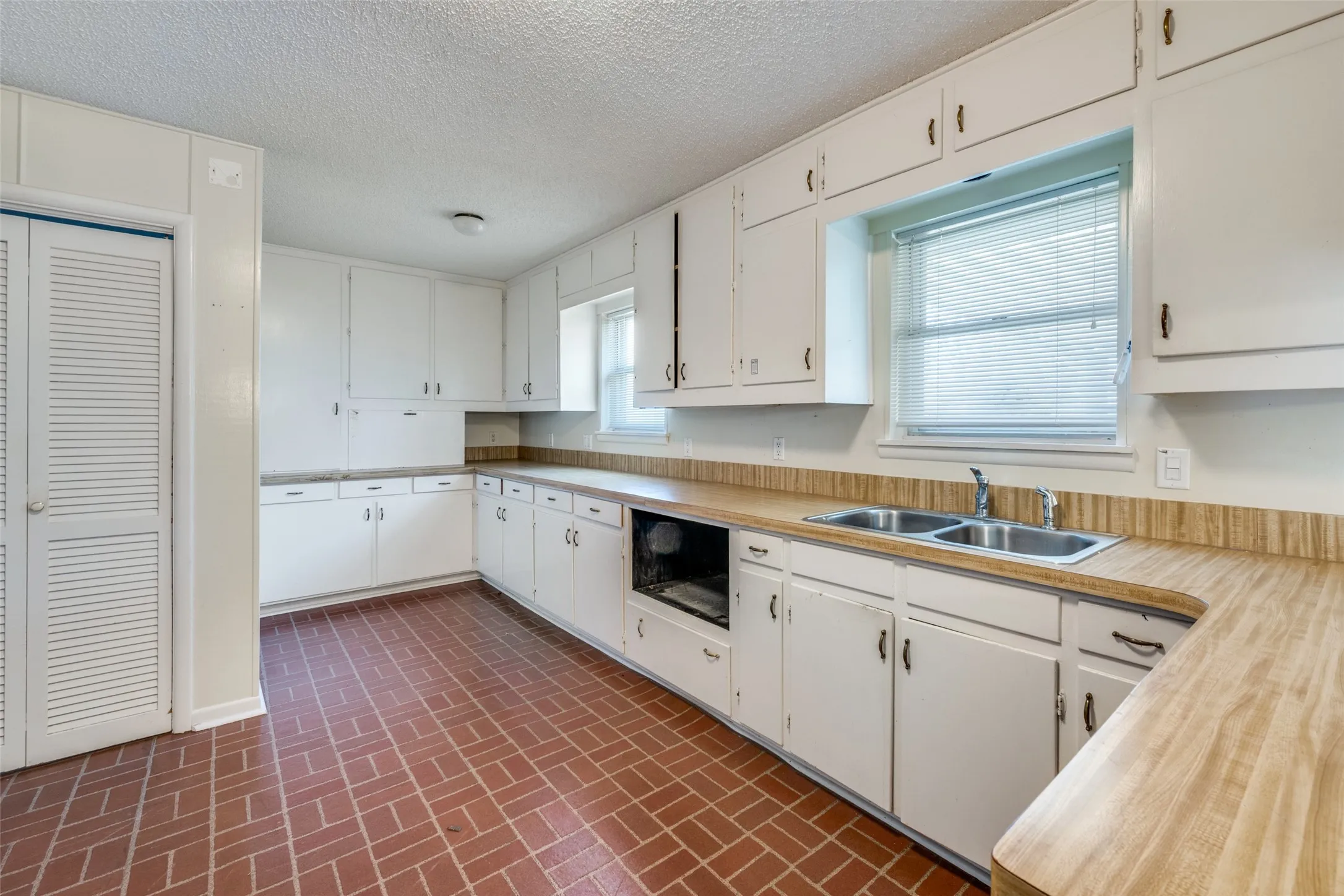 Kitchen featuring abundant white cabinetry, brick-pattern flooring, stainless steel double sink, wood-finish countertops, and built-in wall oven