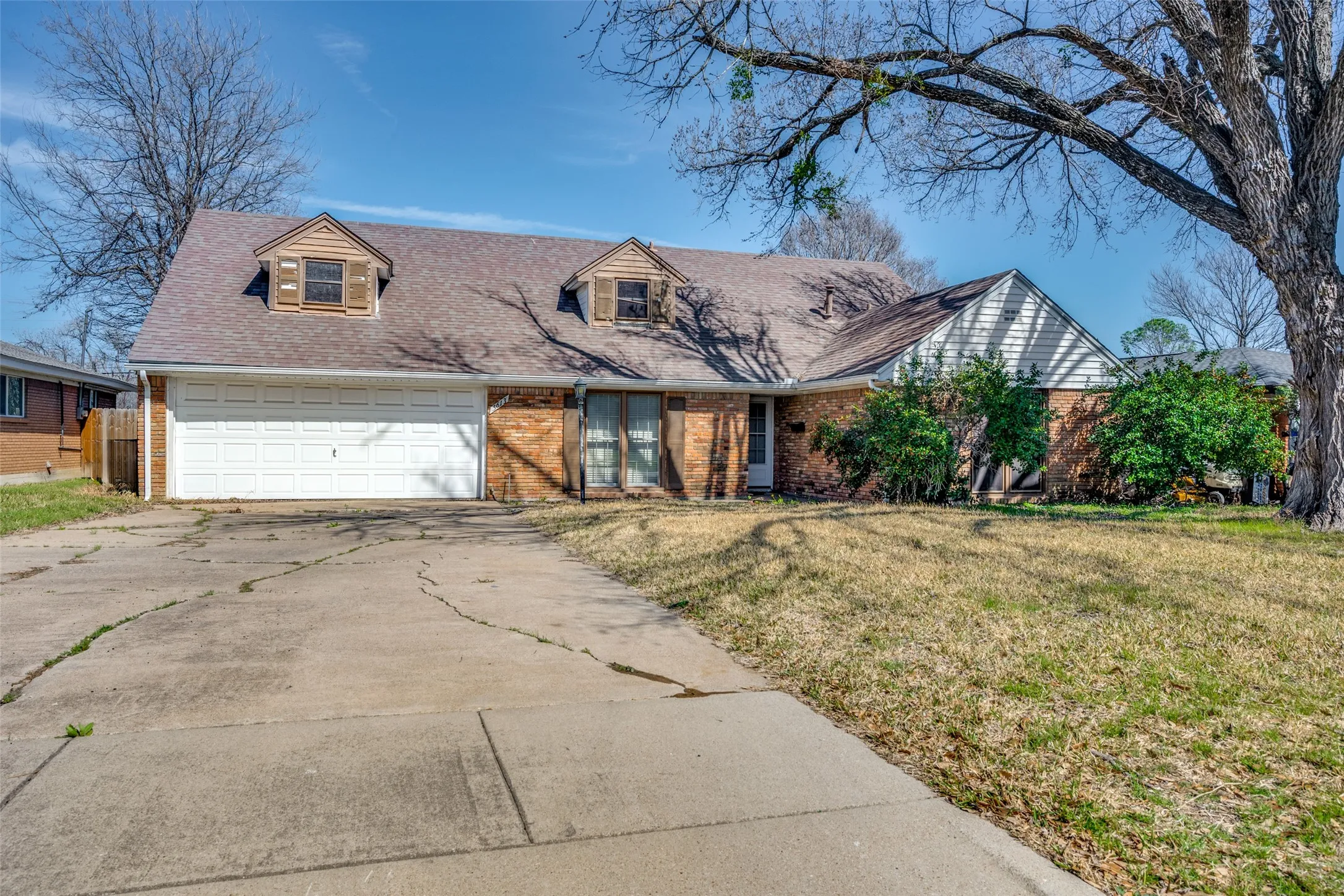 Brick facade home with a two-car garage, dormer windows, and a mature tree