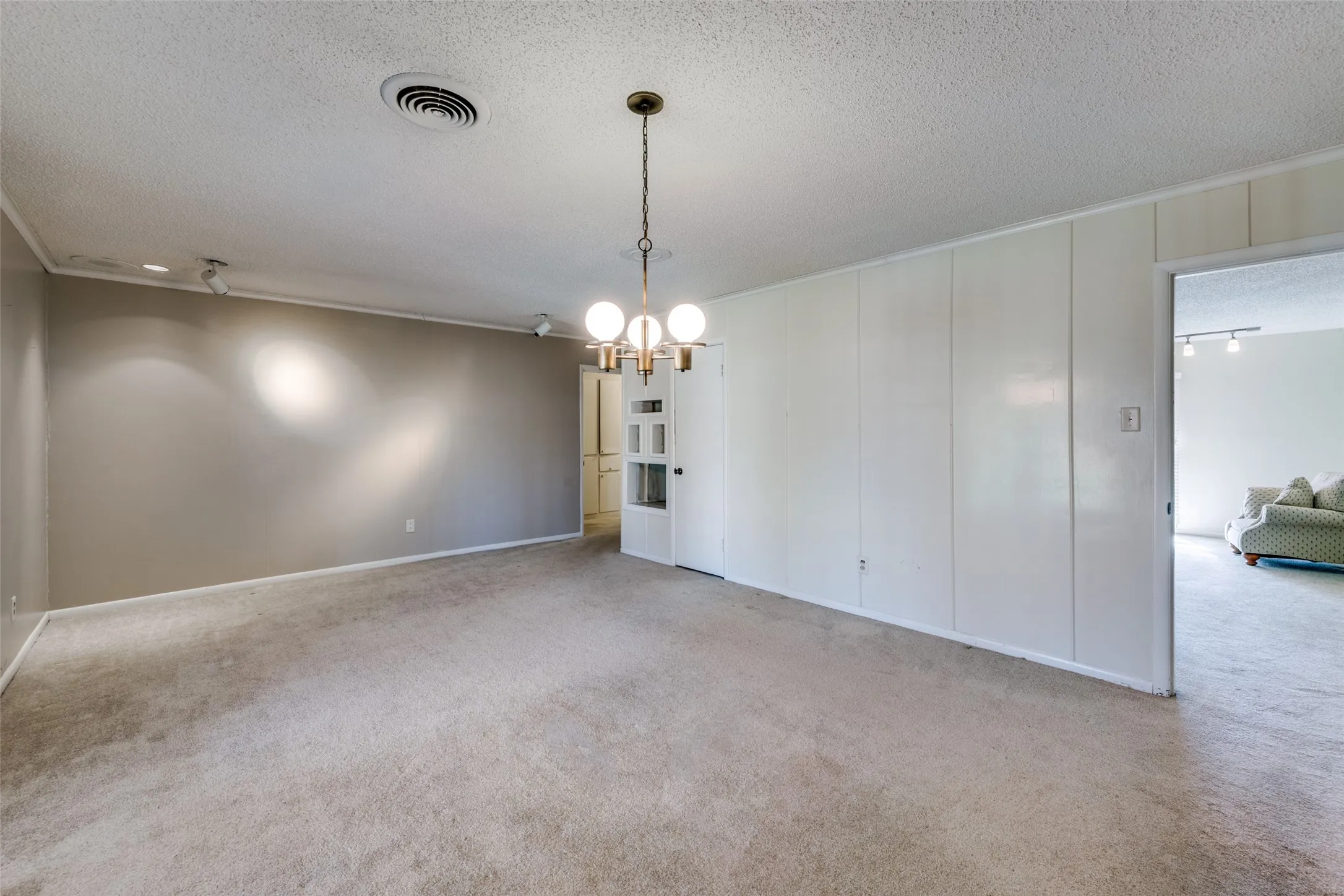 Spacious interior room featuring wall-to-wall carpeting, painted walls, and a multi-bulb chandelier