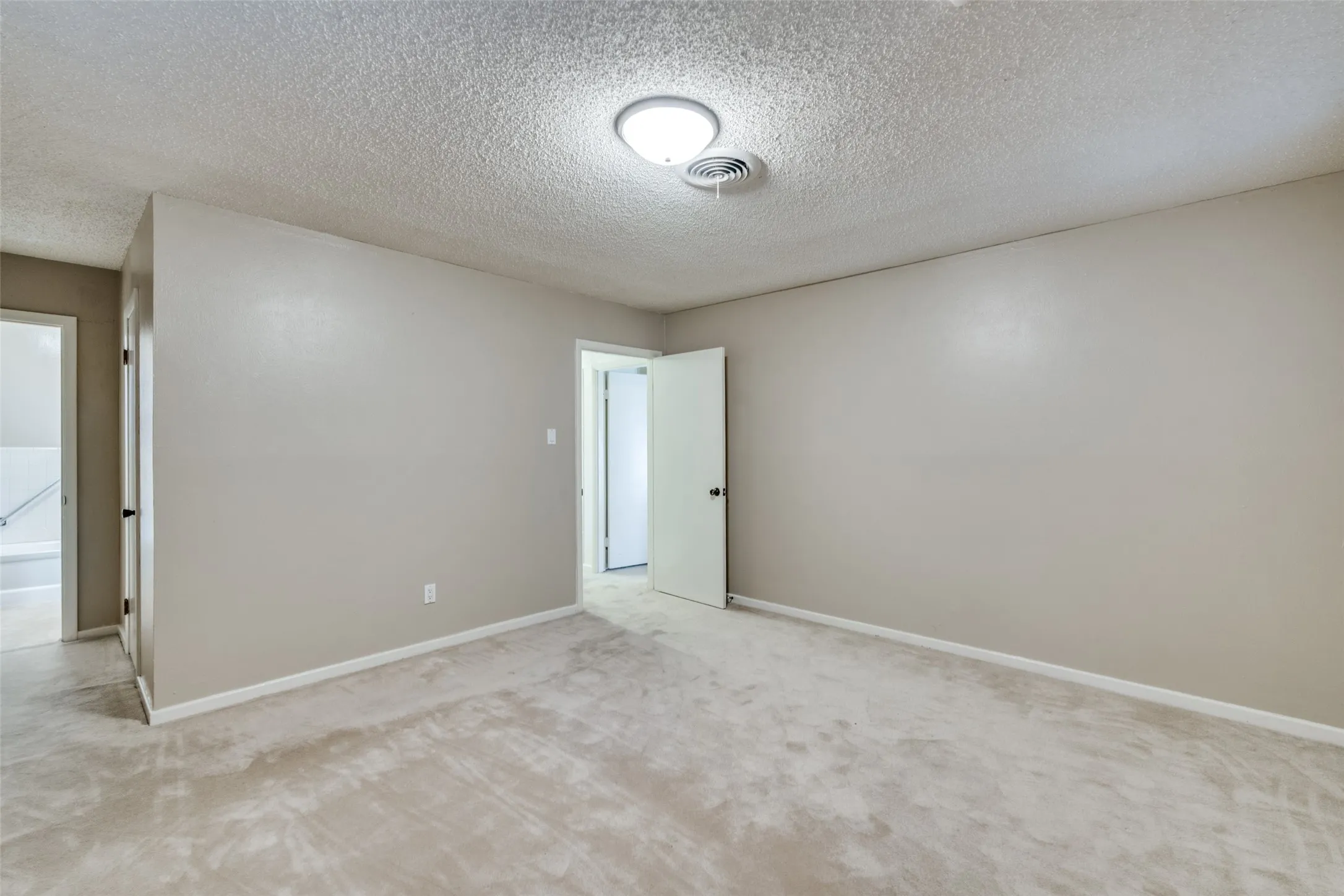 Spacious interior room featuring neutral-toned walls, plush carpeting, and a ceiling-mounted light fixture