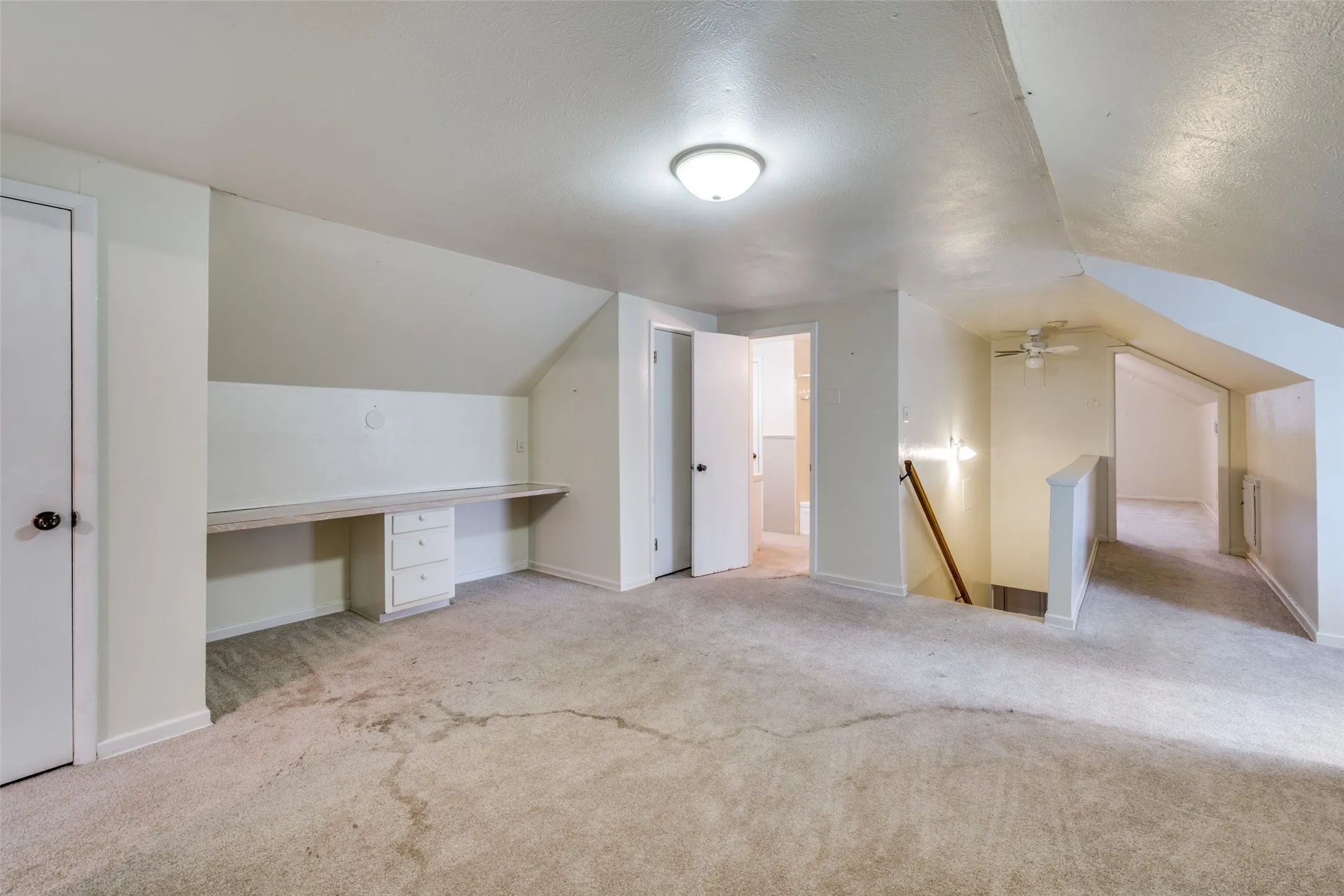Expansive carpeted room featuring a built-in desk with drawers, overhead flush mount lighting, and sloped ceilings