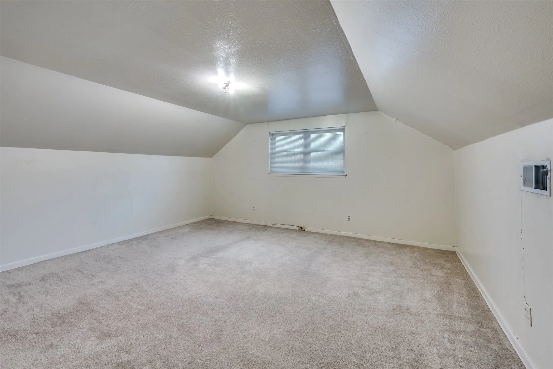 Carpeted room featuring sloped ceilings, a single window with blinds, and white painted walls
