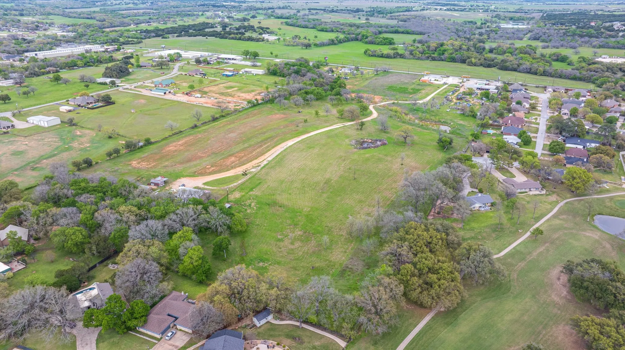 Expansive green space featuring varied topography, mature trees, and unpaved pathways