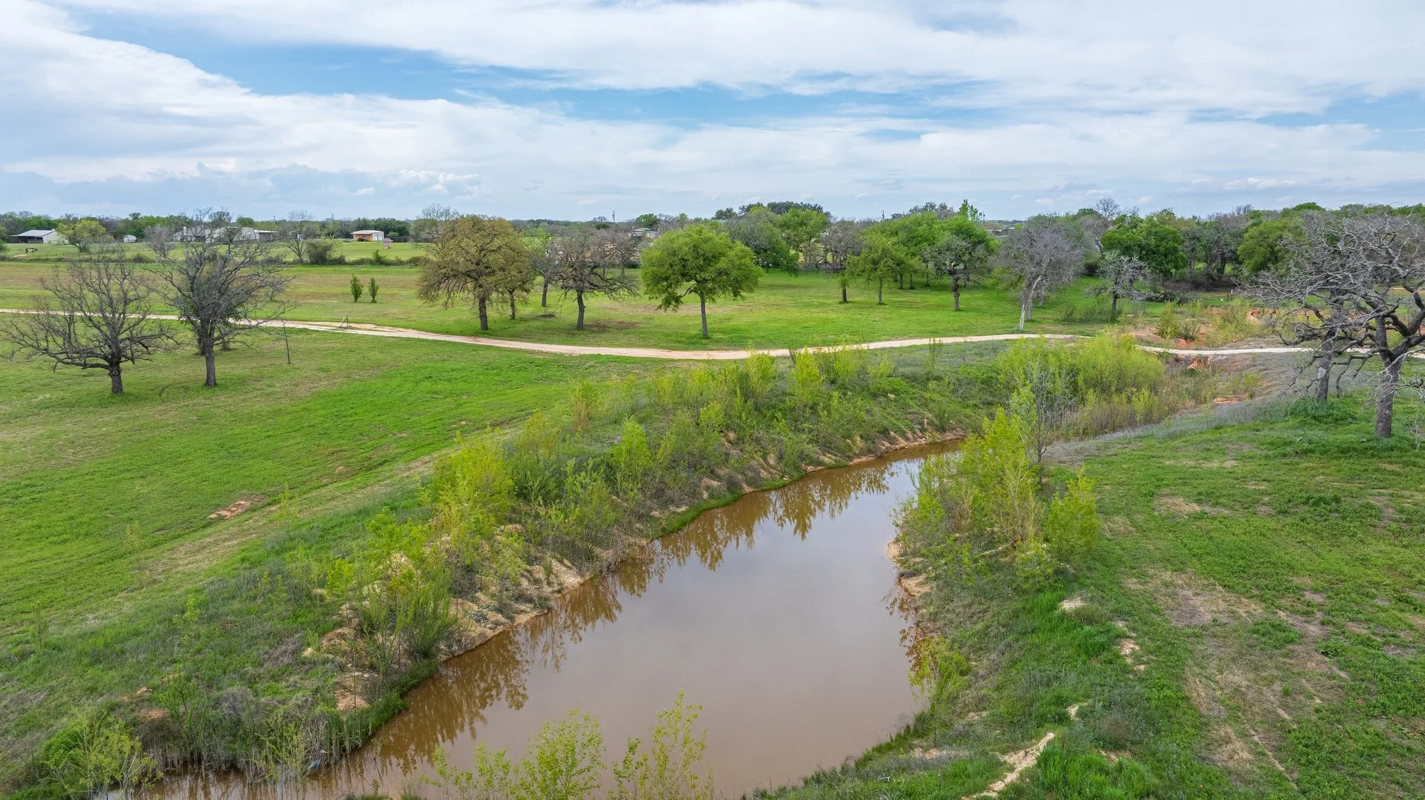 Expansive natural landscape featuring a pond, established trees, a winding dirt path, and open grassy areas