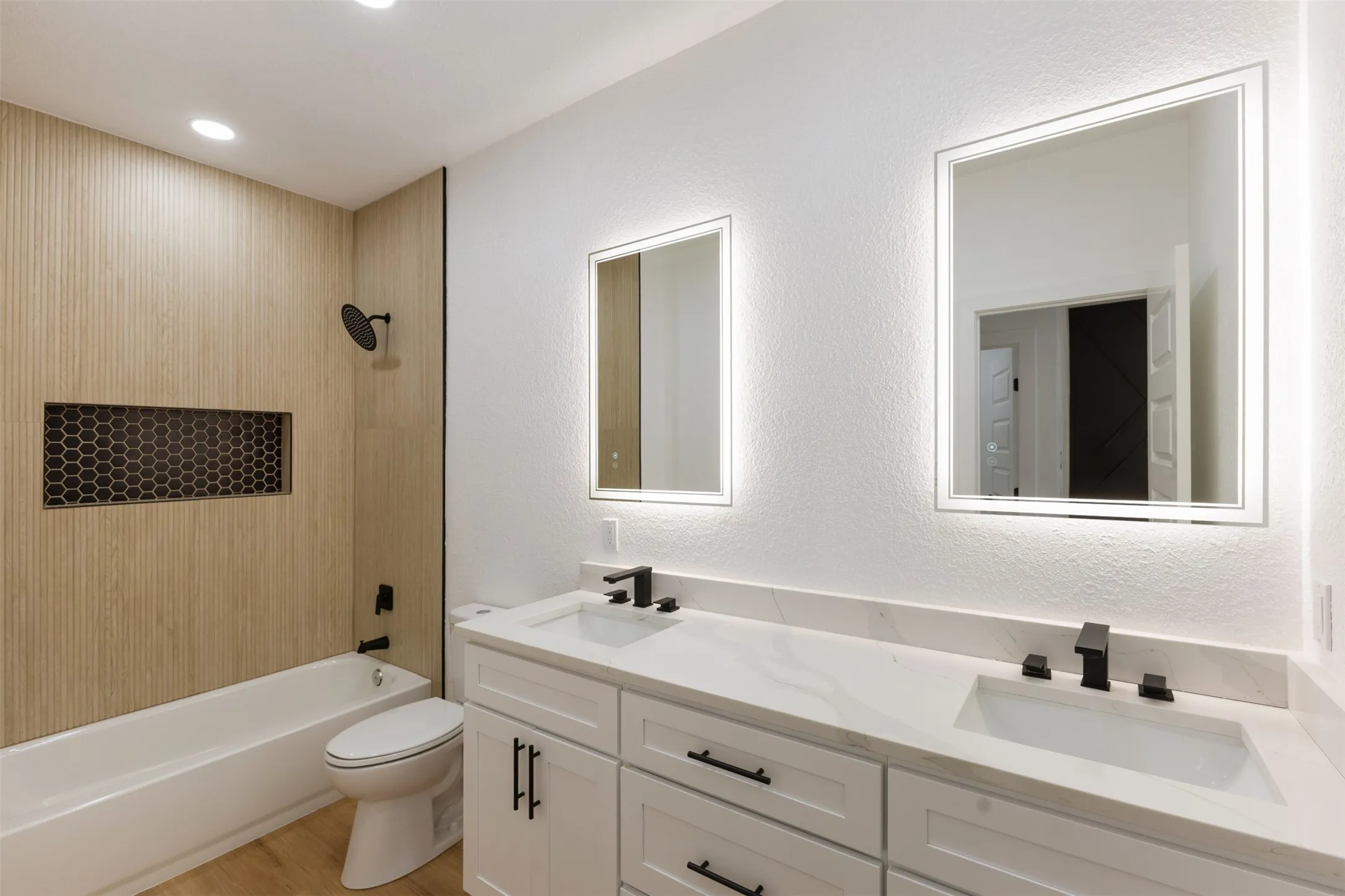 Full bathroom featuring a textured wall, double vanity,  shower combination, and light wood-style flooring