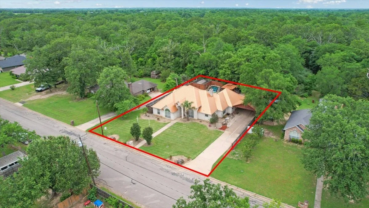 Aerial view of a property featuring a tan-colored house with a multi-gabled roof, an attached carport, and a paved driveway